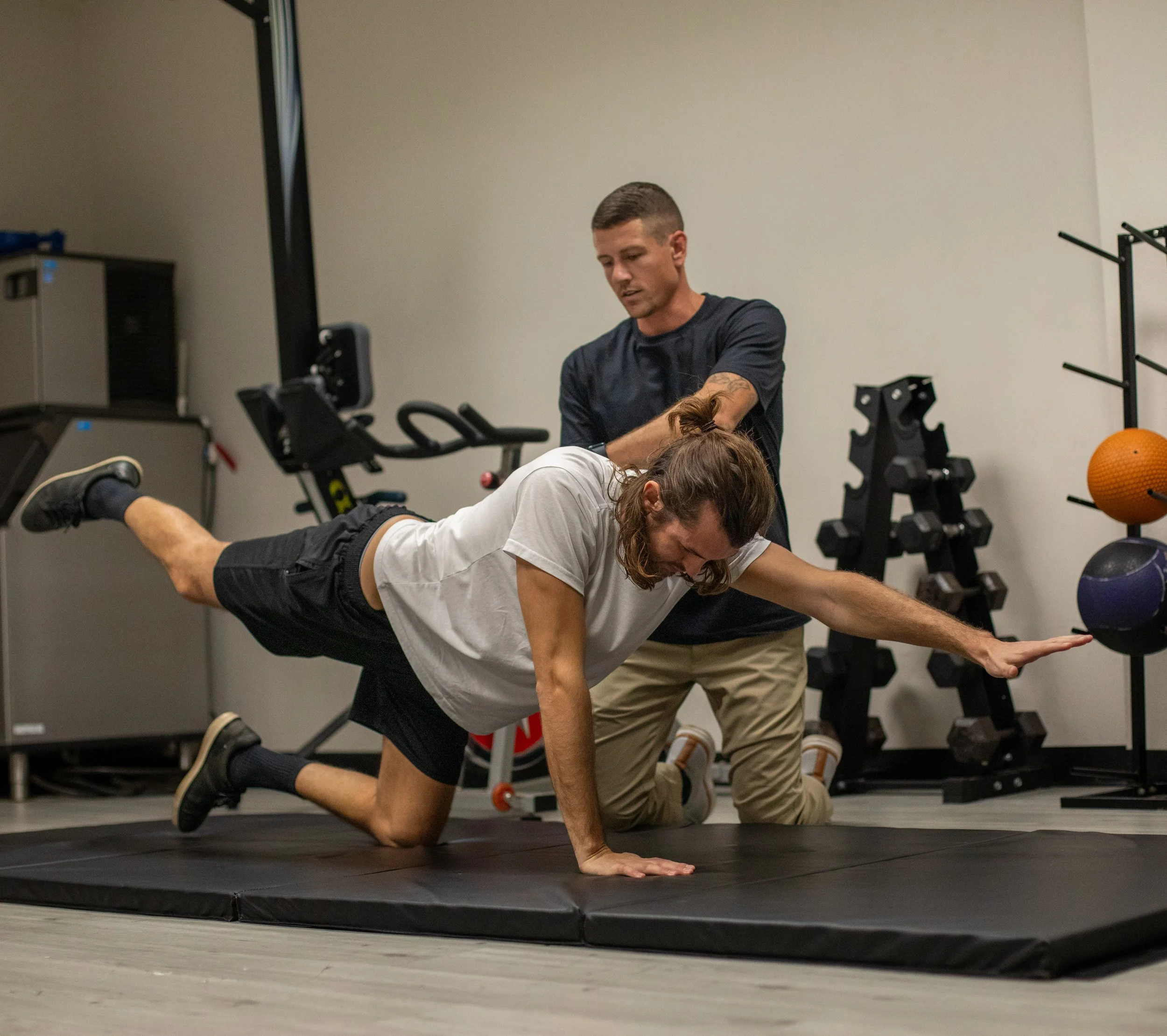 A personal trainer assisting a man performing a push-up in a gym.