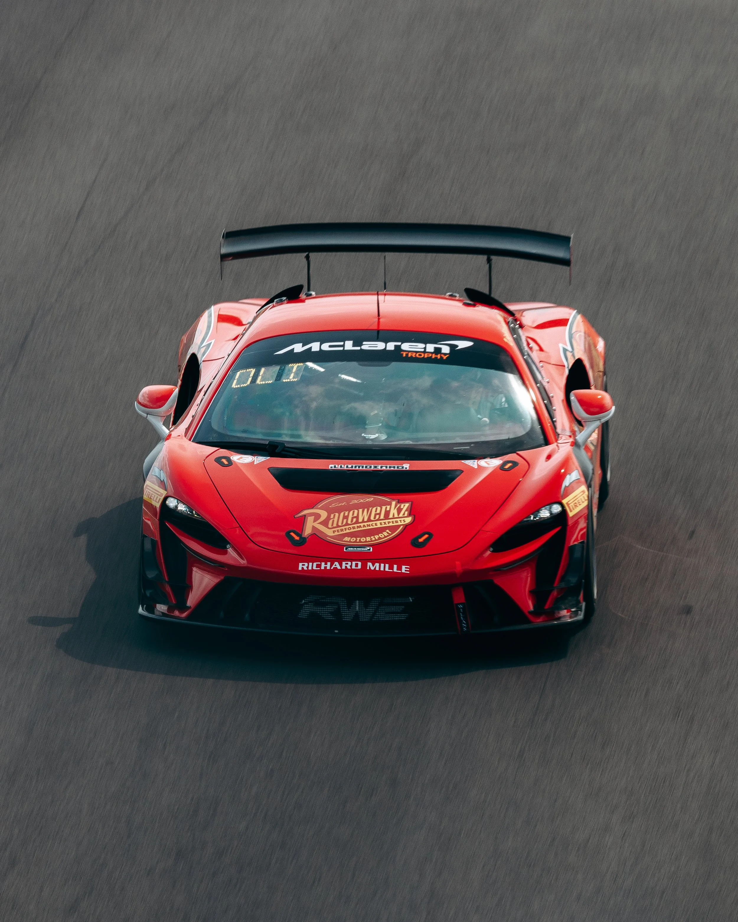 A red McLaren race car driving on a track, viewed from above.