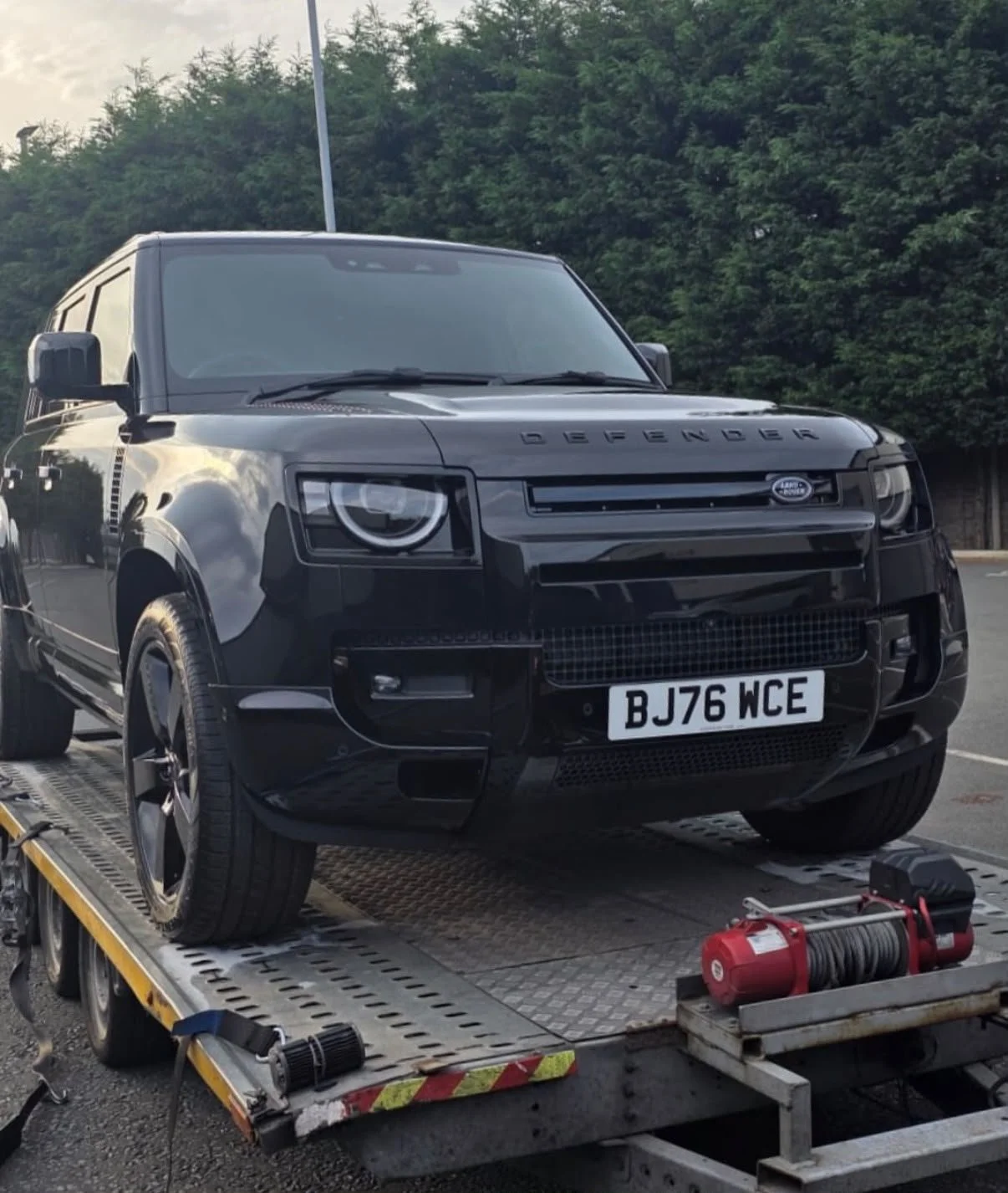A black Land Rover Defender SUV on a flatbed tow truck.