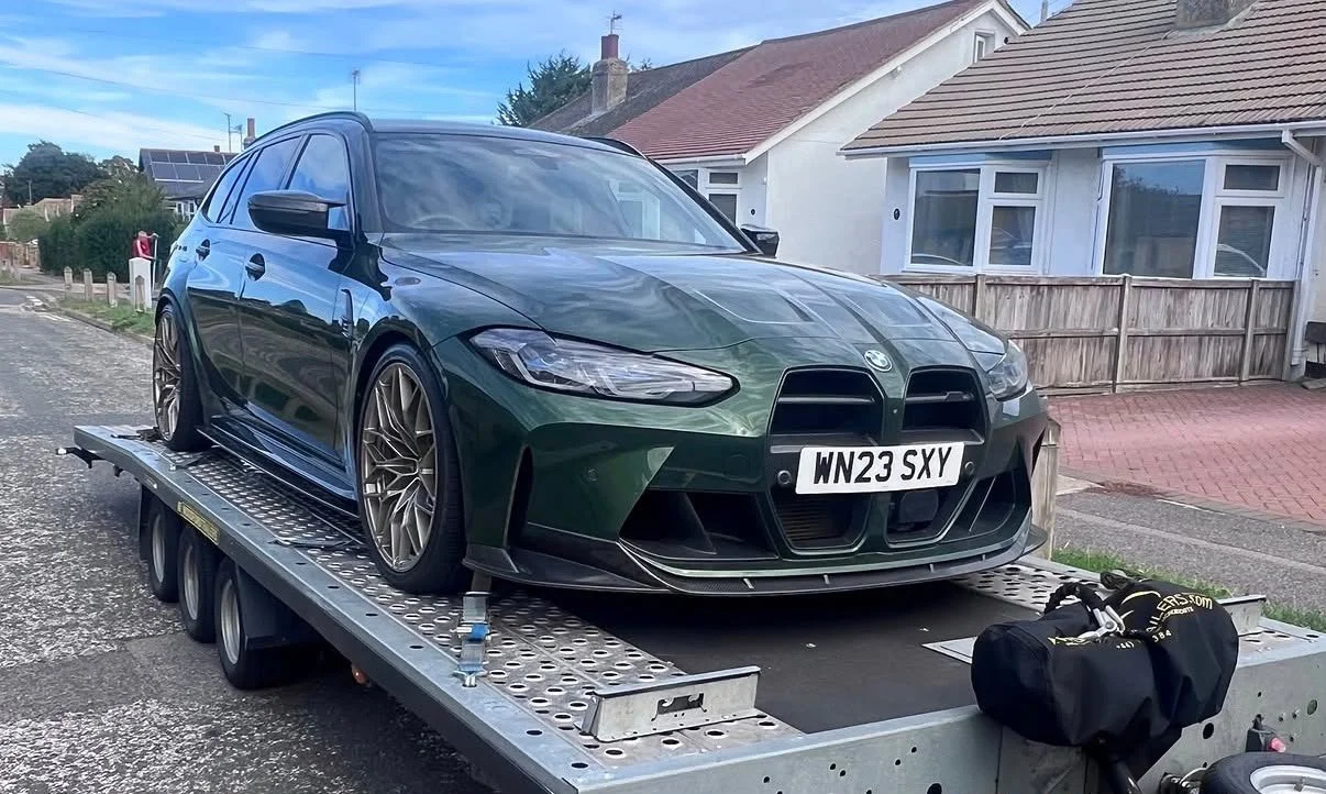 A dark green BMW sports car parked on a flatbed trailer on a residential street.