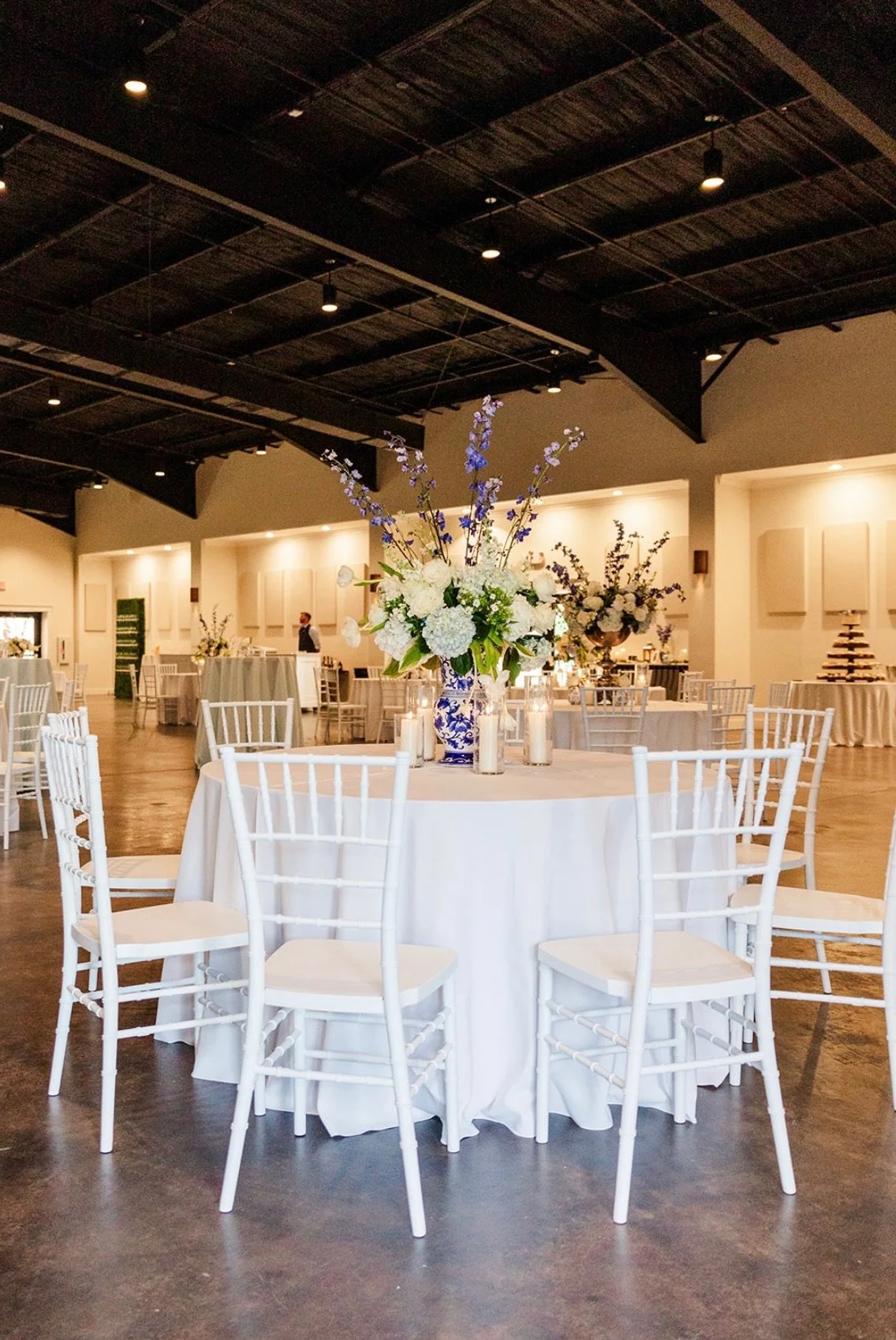 Elegant event space with round table, white tablecloth, and floral centerpiece with white and purple flowers.