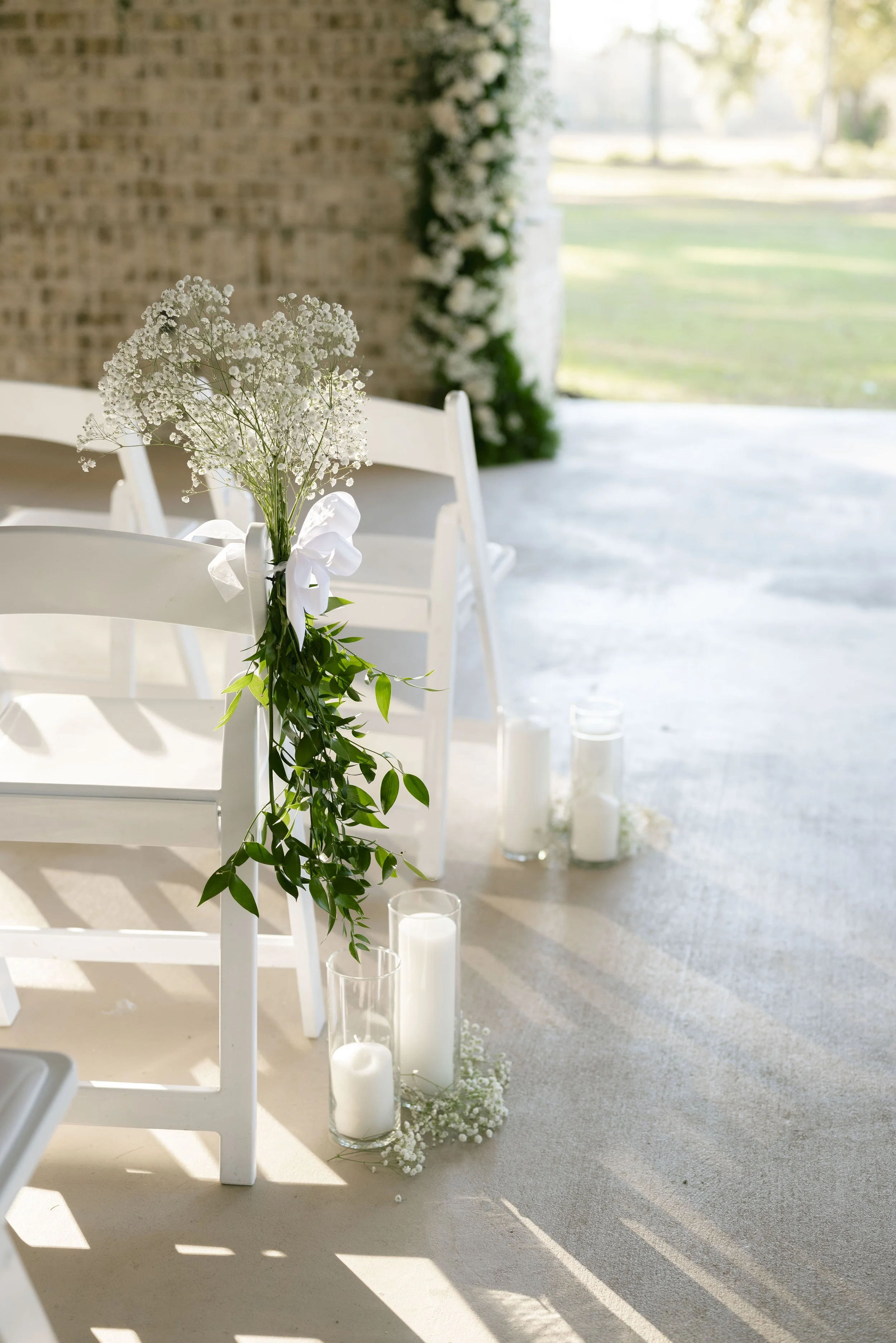 White chairs decorated with flowers and candles, set up for a wedding ceremony outdoors.