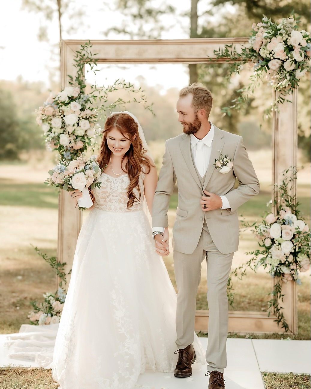 A newlywed couple walking hand in hand down an outdoor aisle decorated with flowers during a wedding ceremony.