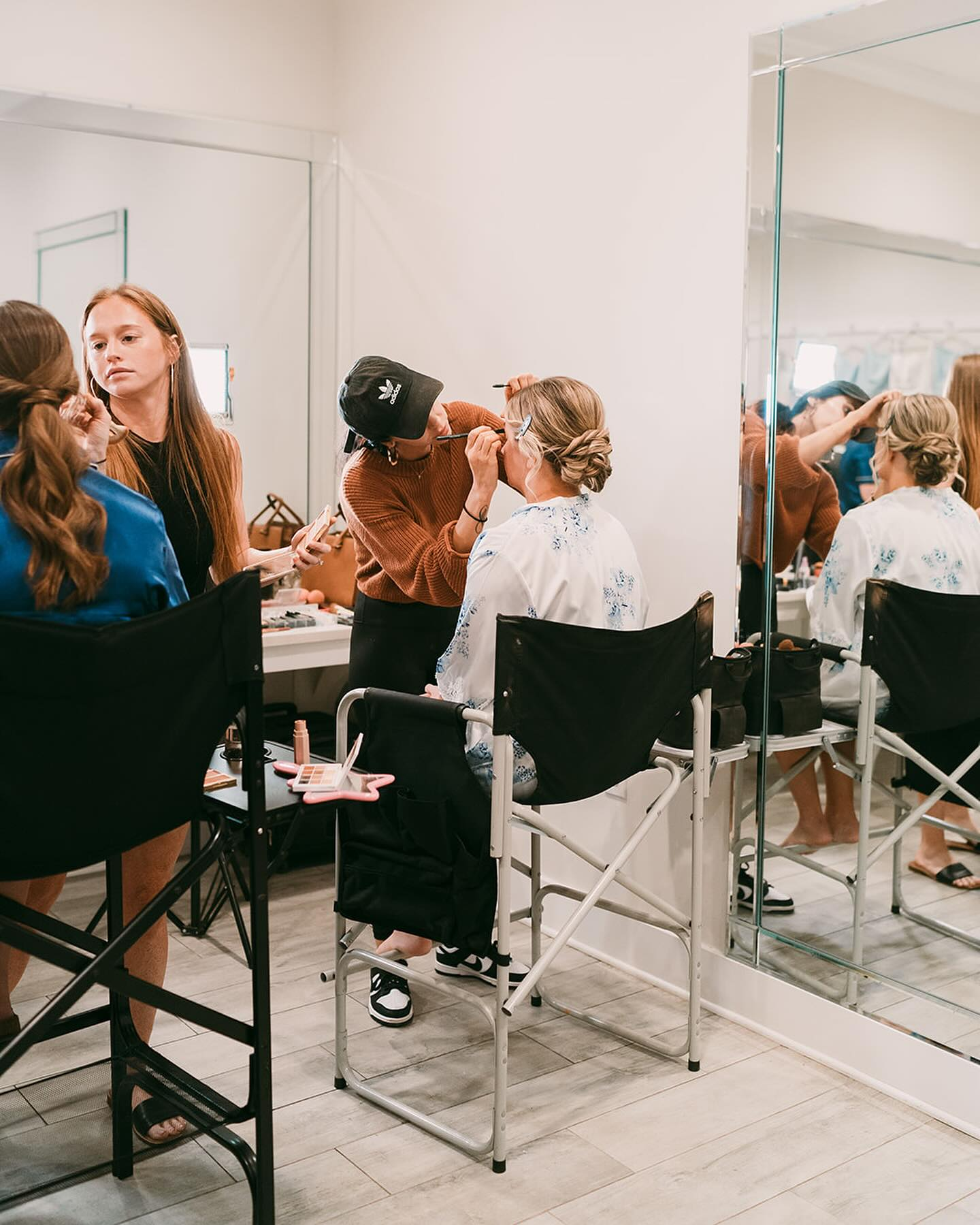 Makeup artist applying makeup on a woman seated in front of a mirror.