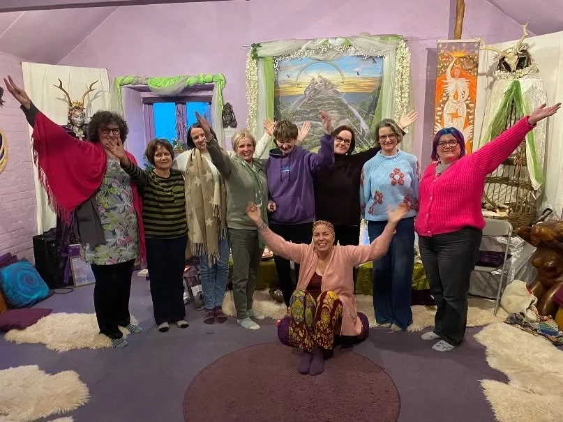 Group of nine women posing and smiling in a colorful, eclectic room with art and decorations.