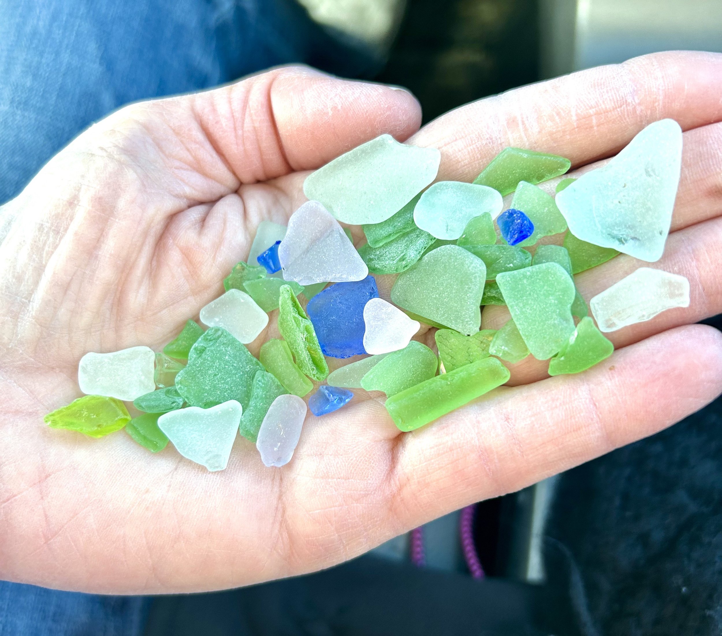 A person's hand holding small pieces of sea glass in shades of green, blue, and white.