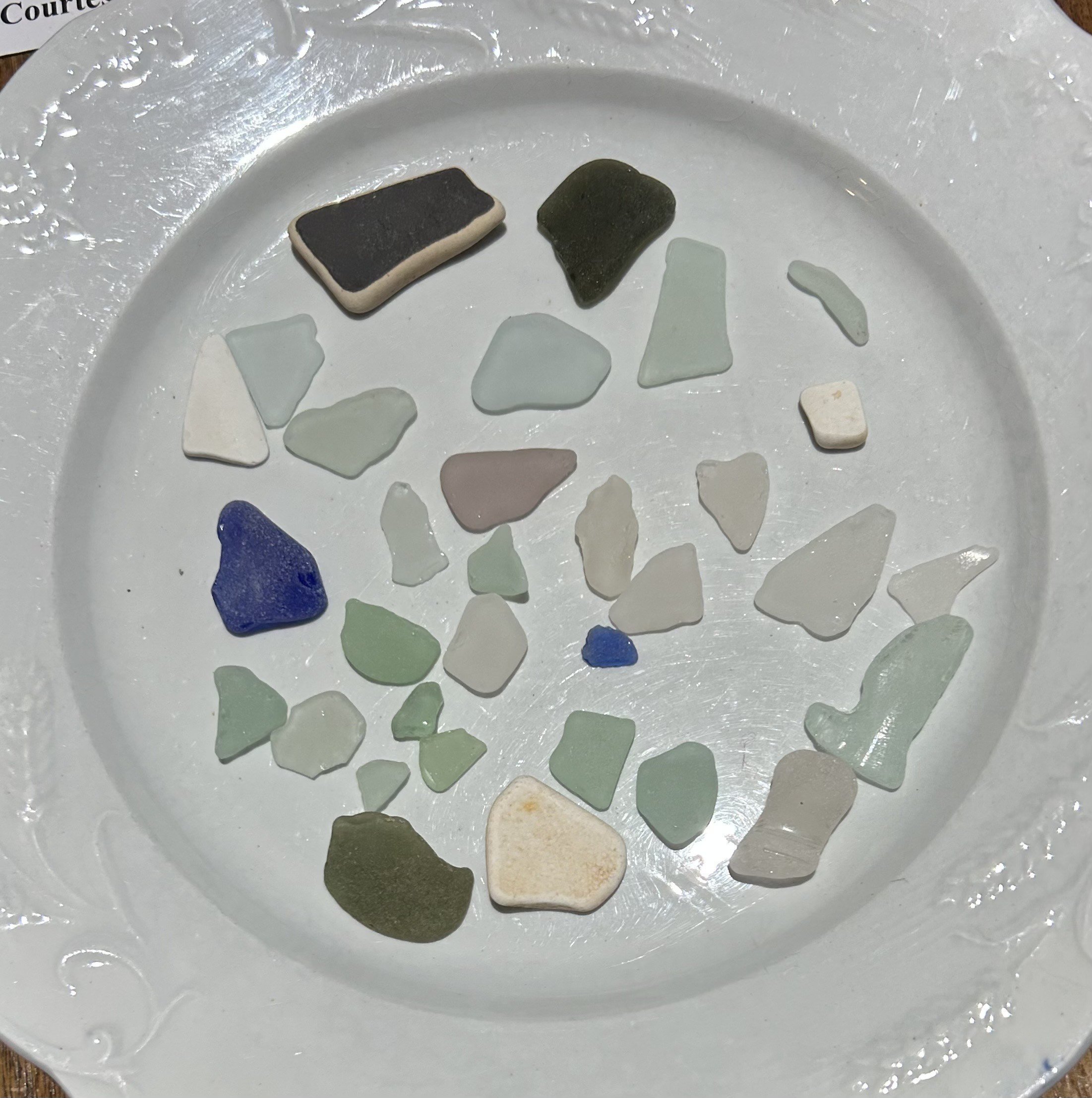 Collection of small, colorful sea glass pieces on a white decorative plate.