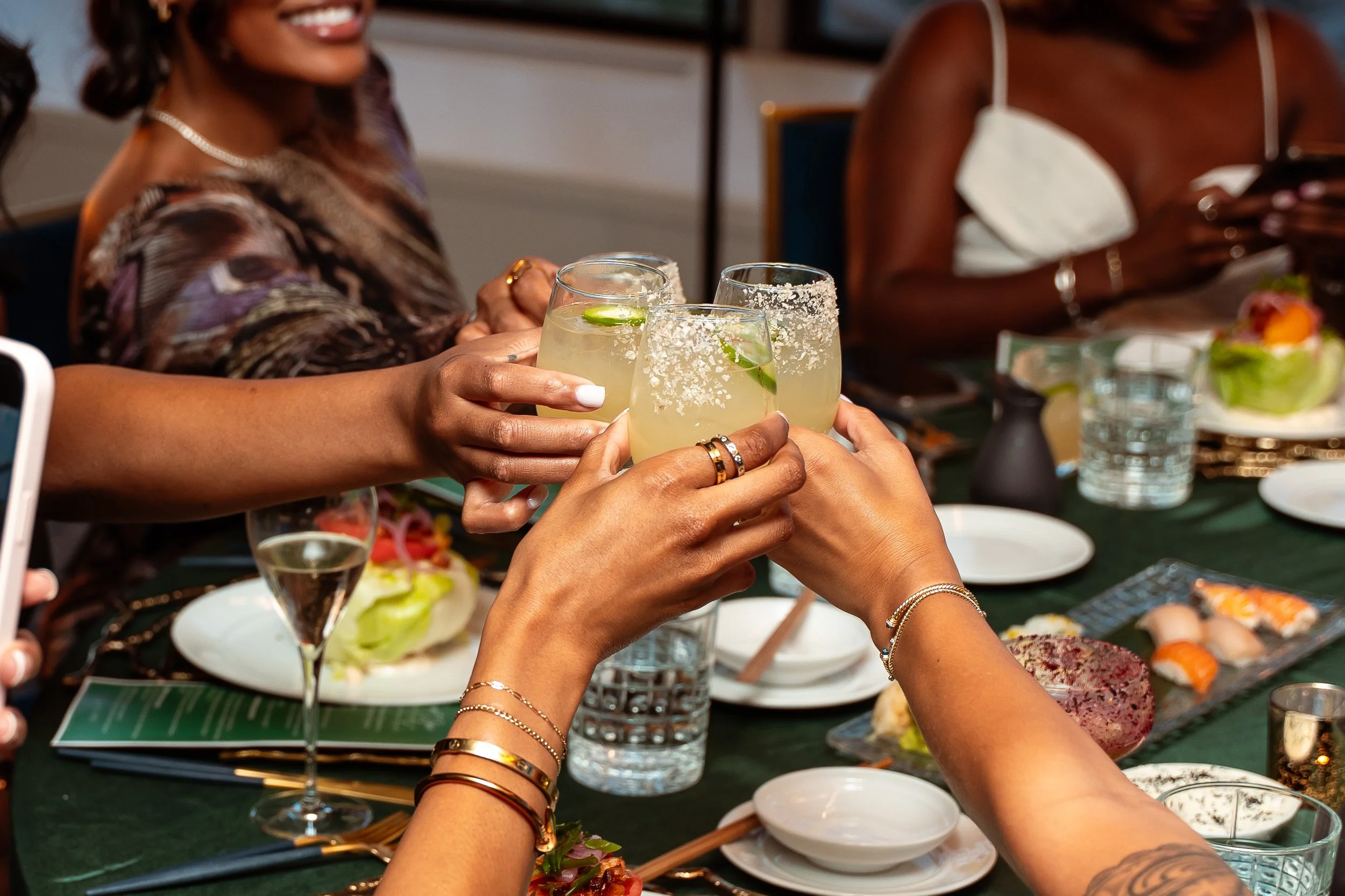 People sitting at a table making a toast with margarita glasses garnished with lime slices.