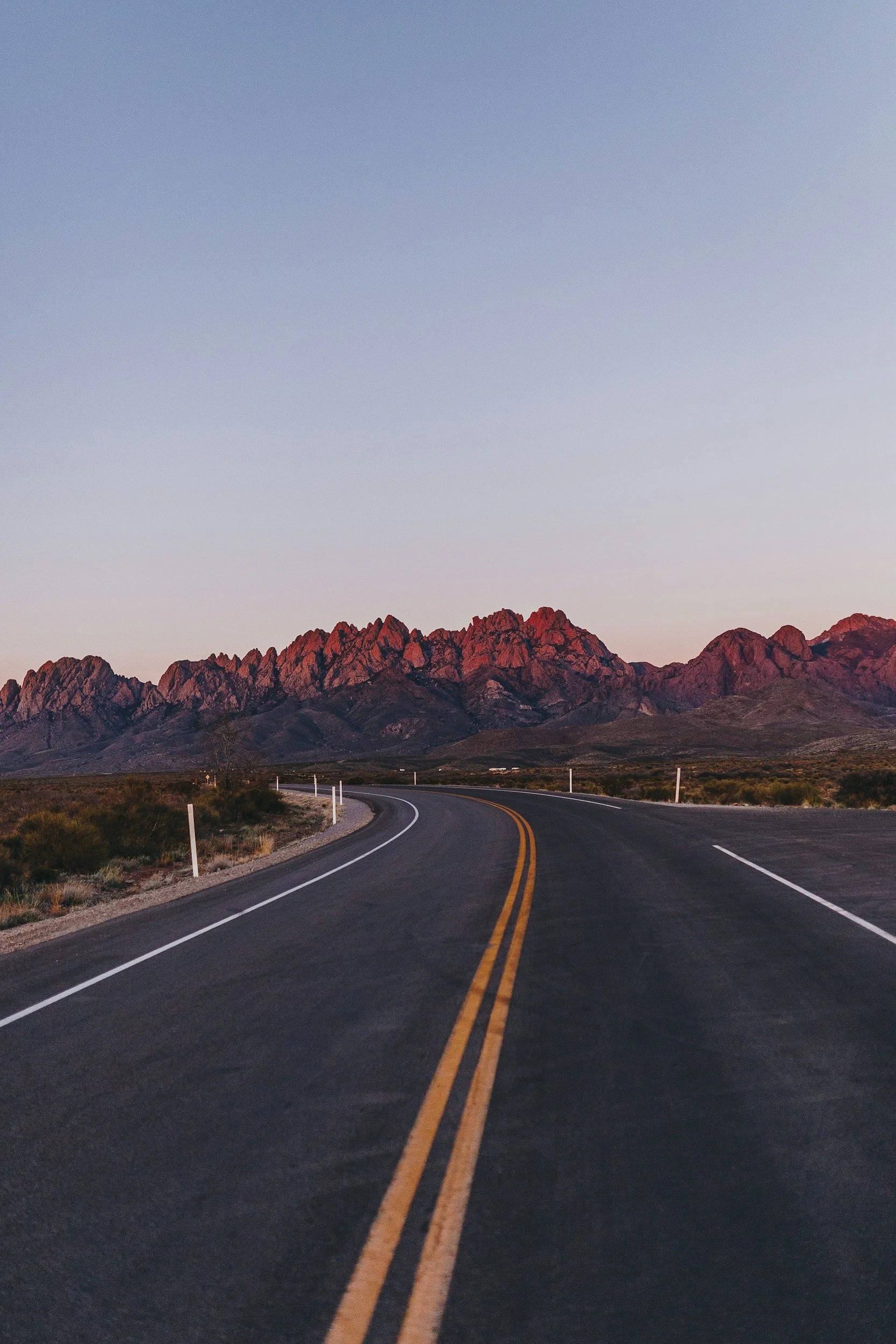 Open desert highway with mountains in the background at sunset.