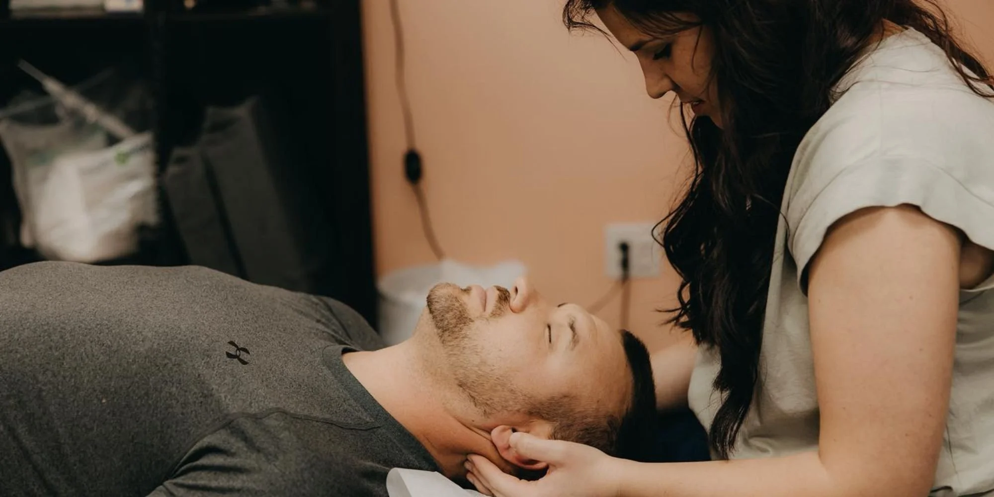 A woman leaning over a man lying in bed, holding his head and looking into his eyes.
