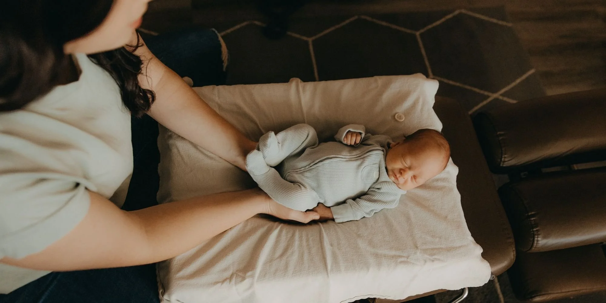 People holding a newborn baby dressed in gray, lying on a cushioned changing pad.