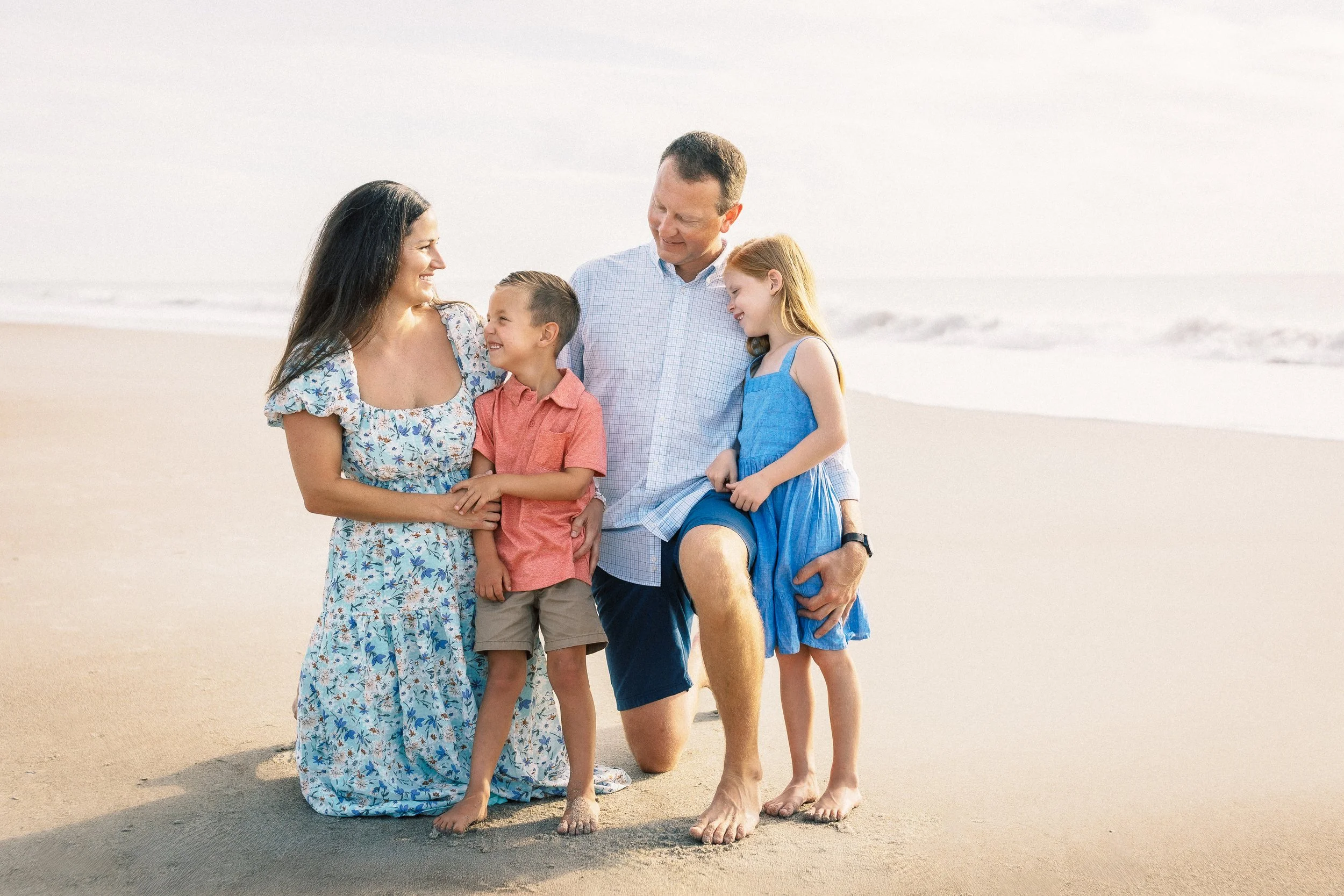 Family of four standing on the beach, smiling and enjoying a moment together, with the ocean in the background.Photographer Amelia Island, Jacksonville, St Augustine, St Simons Island, Savannah photographer