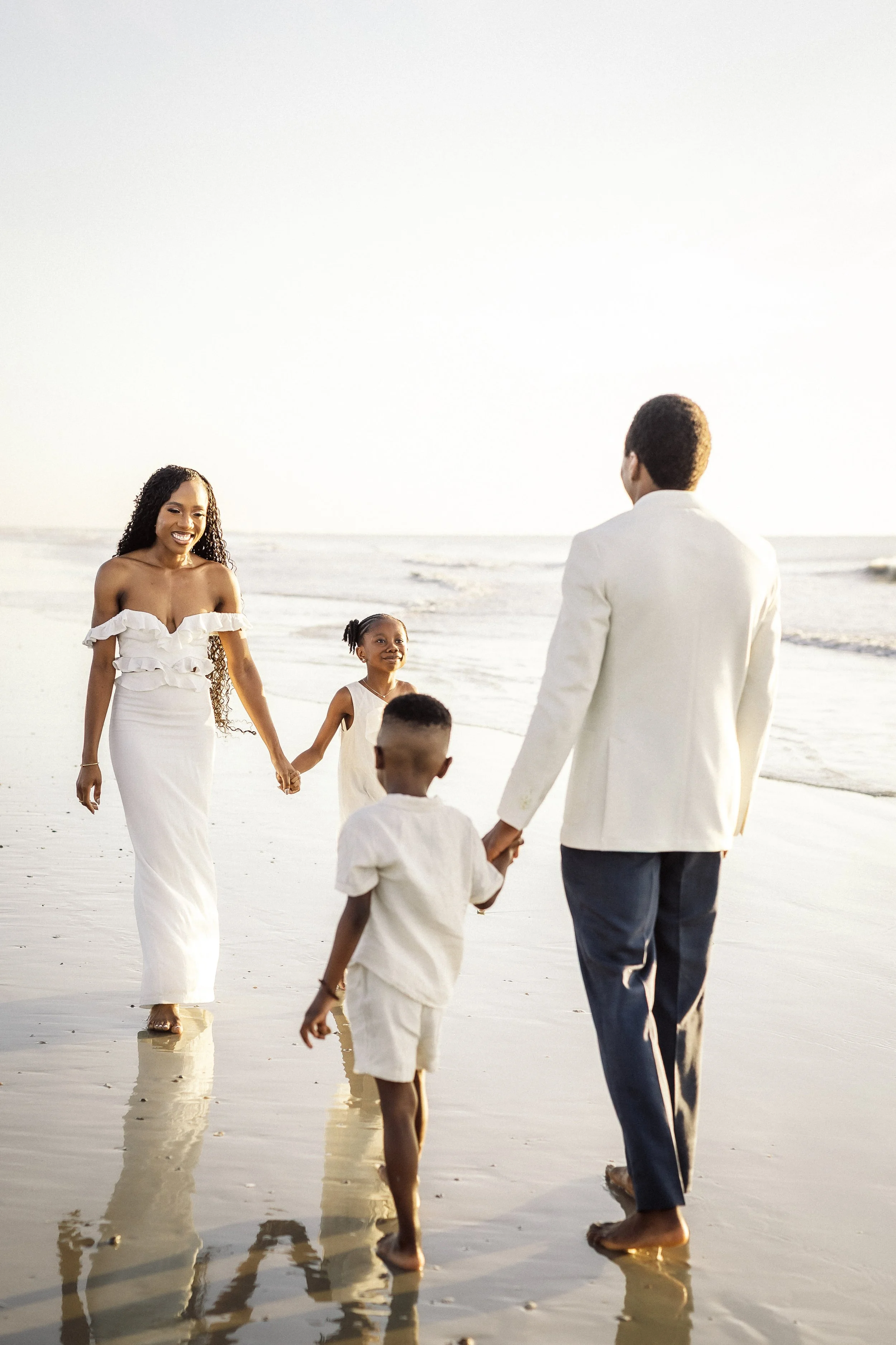 A family enjoying a walk on the beach during sunset, holding hands and smiling.