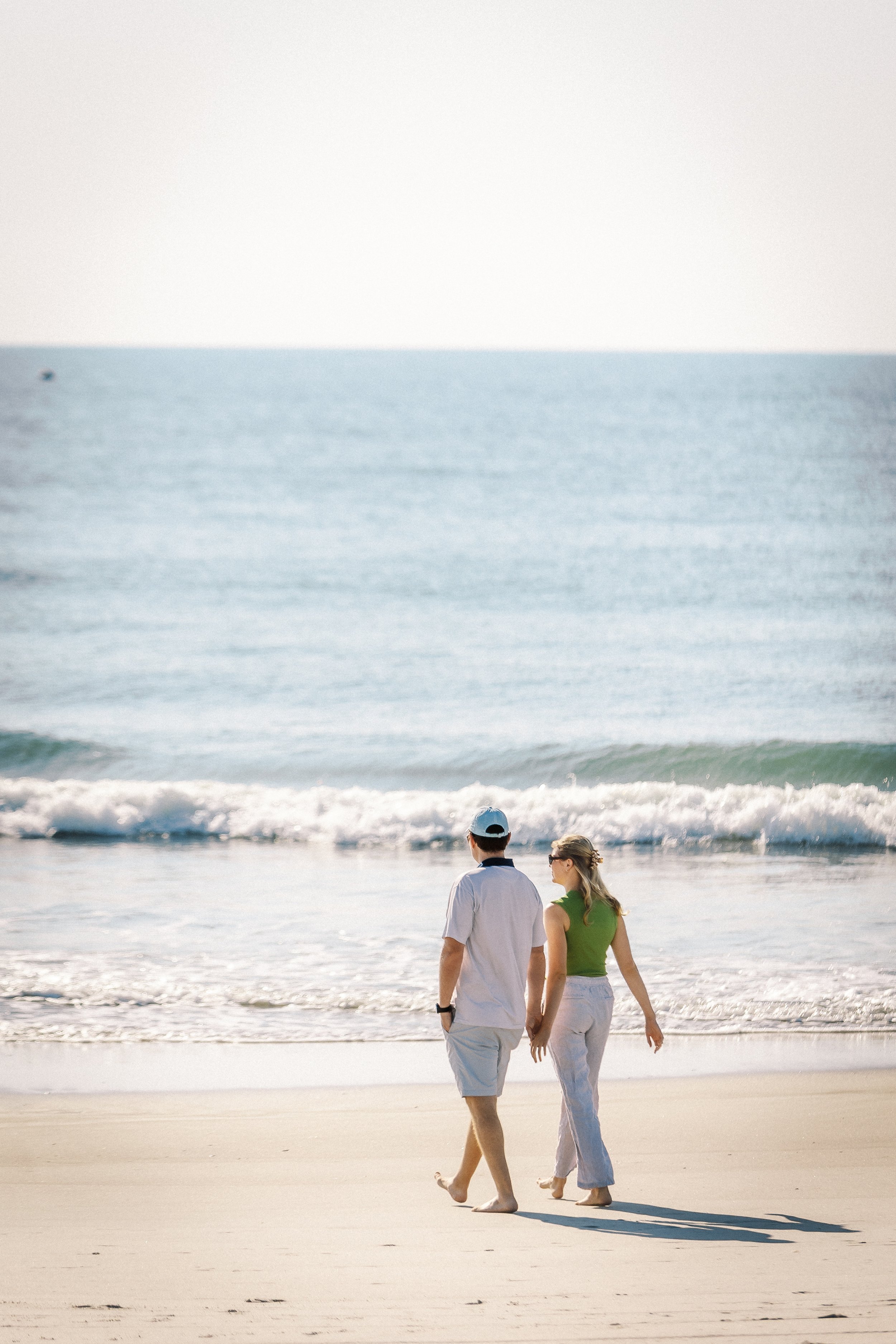 A couple walking along the beach near the shoreline with waves.