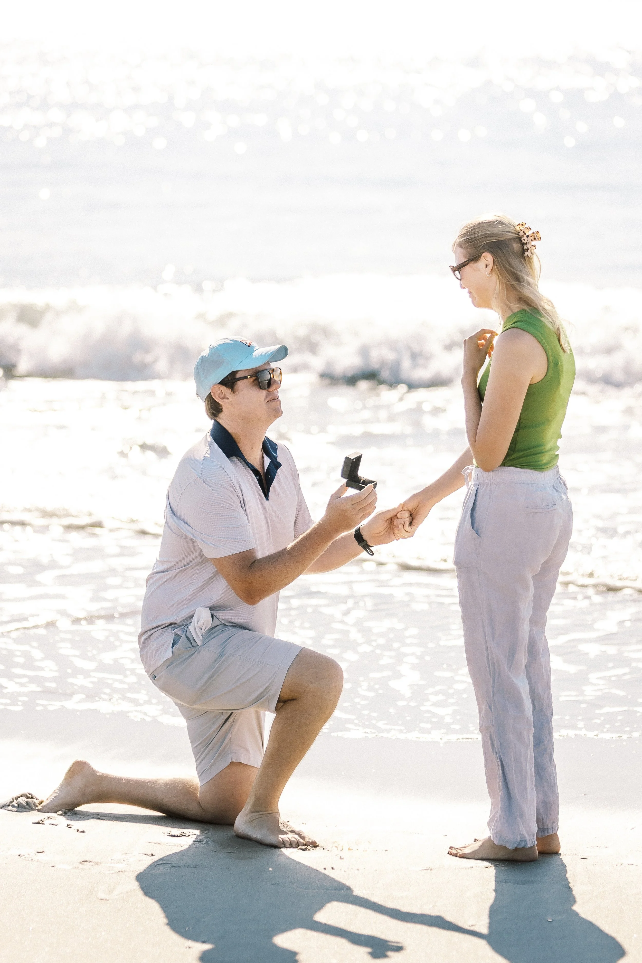 Kneeling man proposing to woman on a beach during sunset