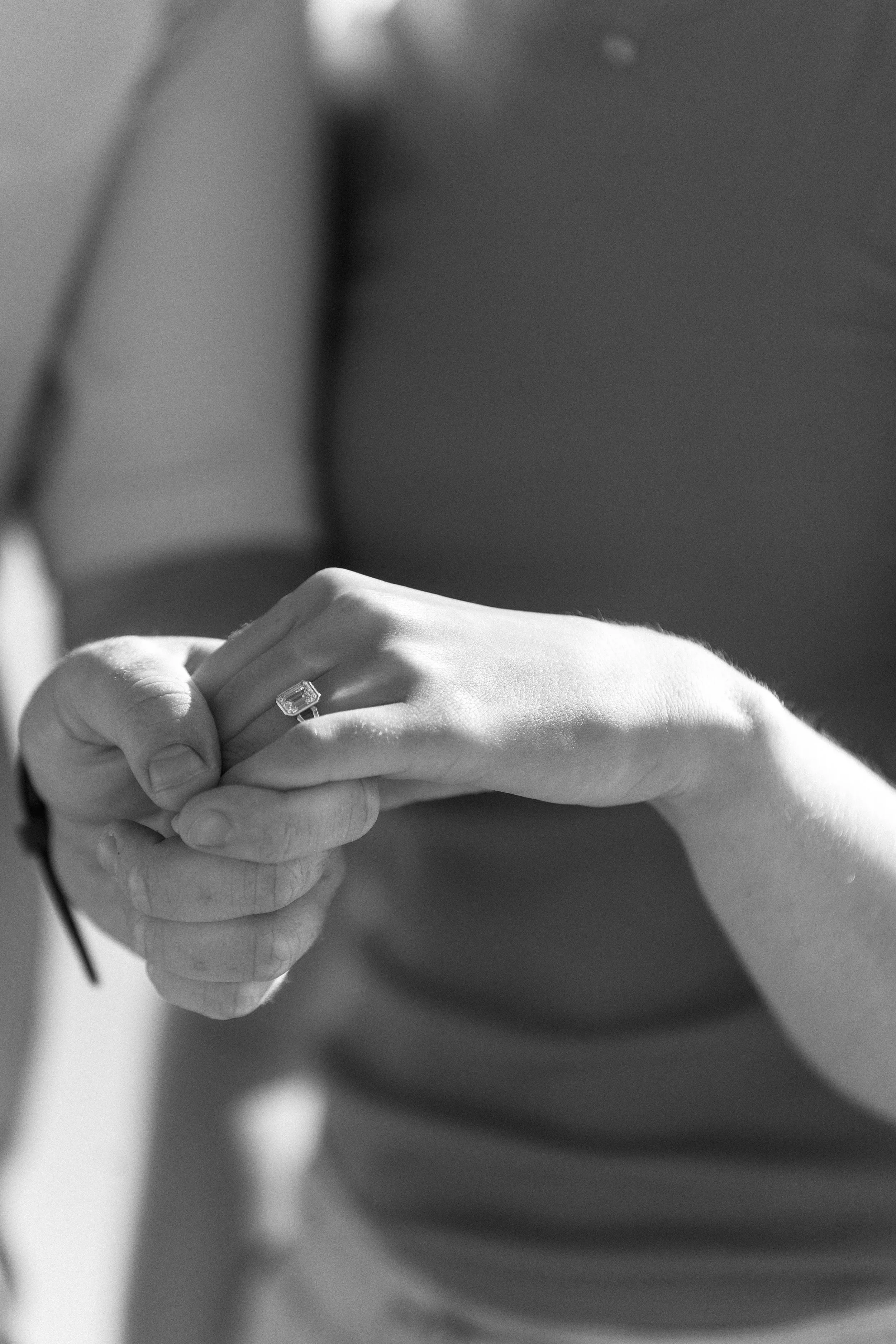 Close-up of a person's hand holding a pair of eyeglasses, wearing a ring with a rectangular gemstone.