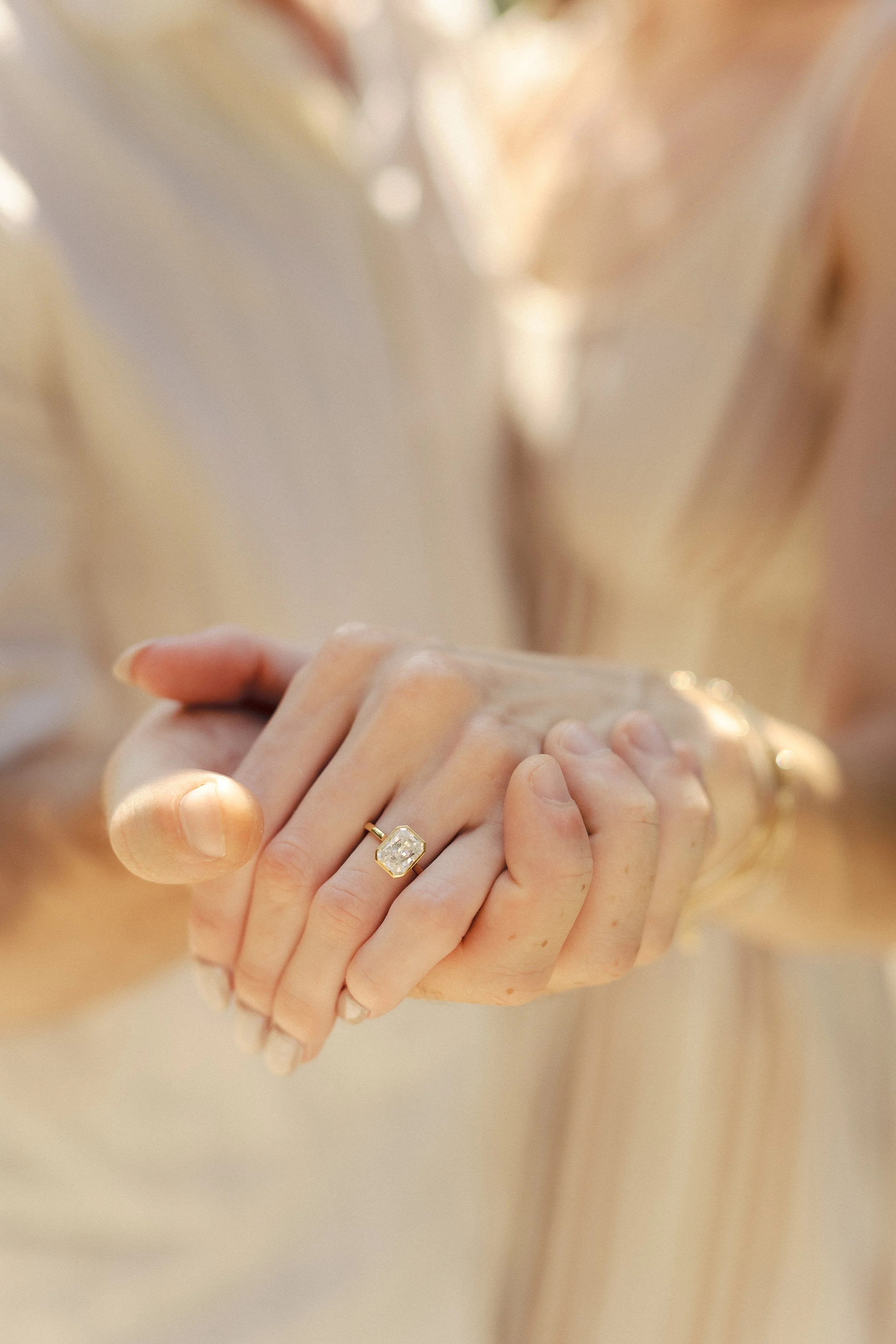 Close-up of a person holding a gemstone ring with both hands, showing skin and nails, with a blurred background.