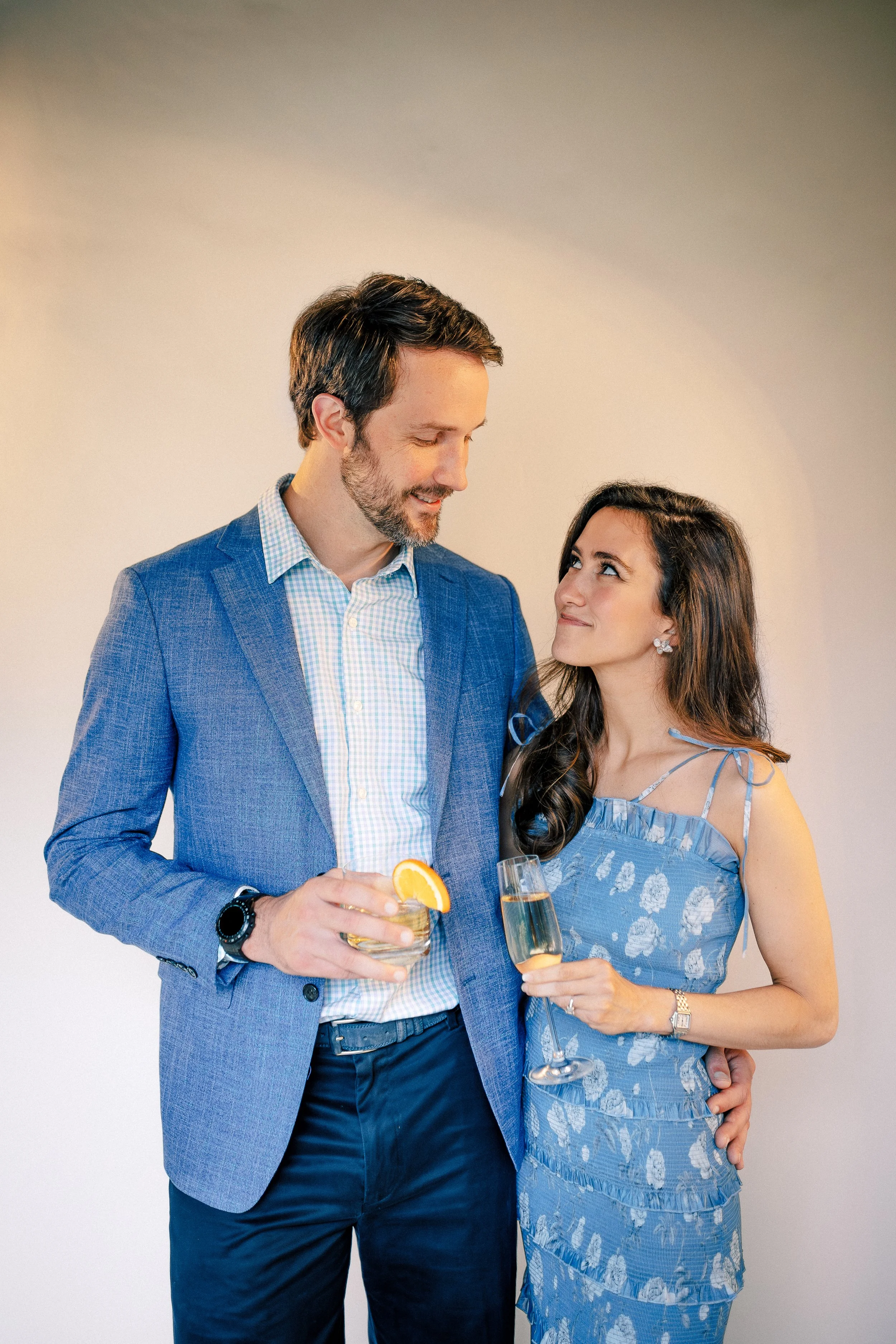 A man and woman at a celebration, holding drinks and looking at each other with smiles.