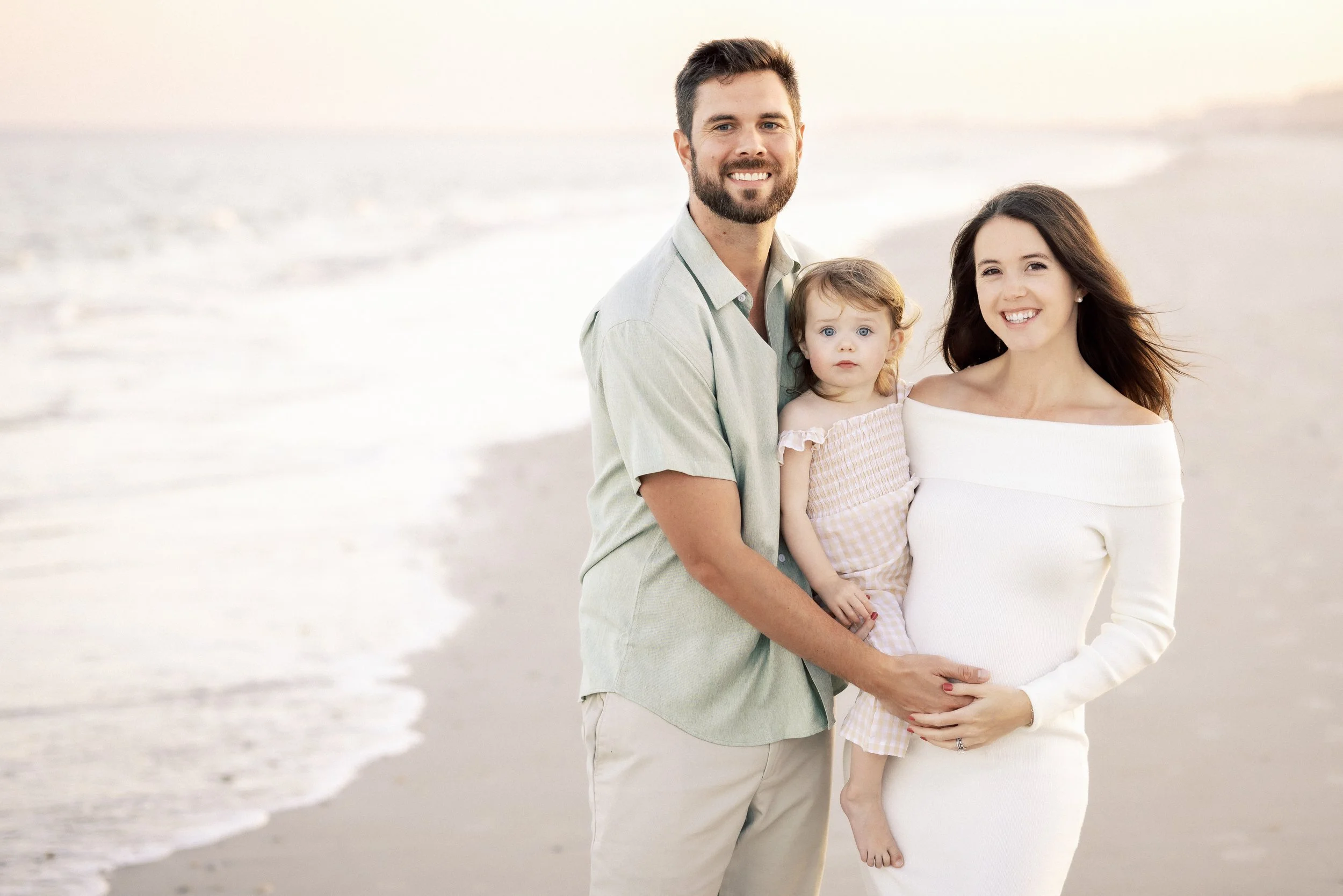 A happy family of three standing on the beach with the ocean in the background, smiling at the camera.Photographer Amelia Island, Jacksonville, St Augustine, St Simons Island, Savannah photographer