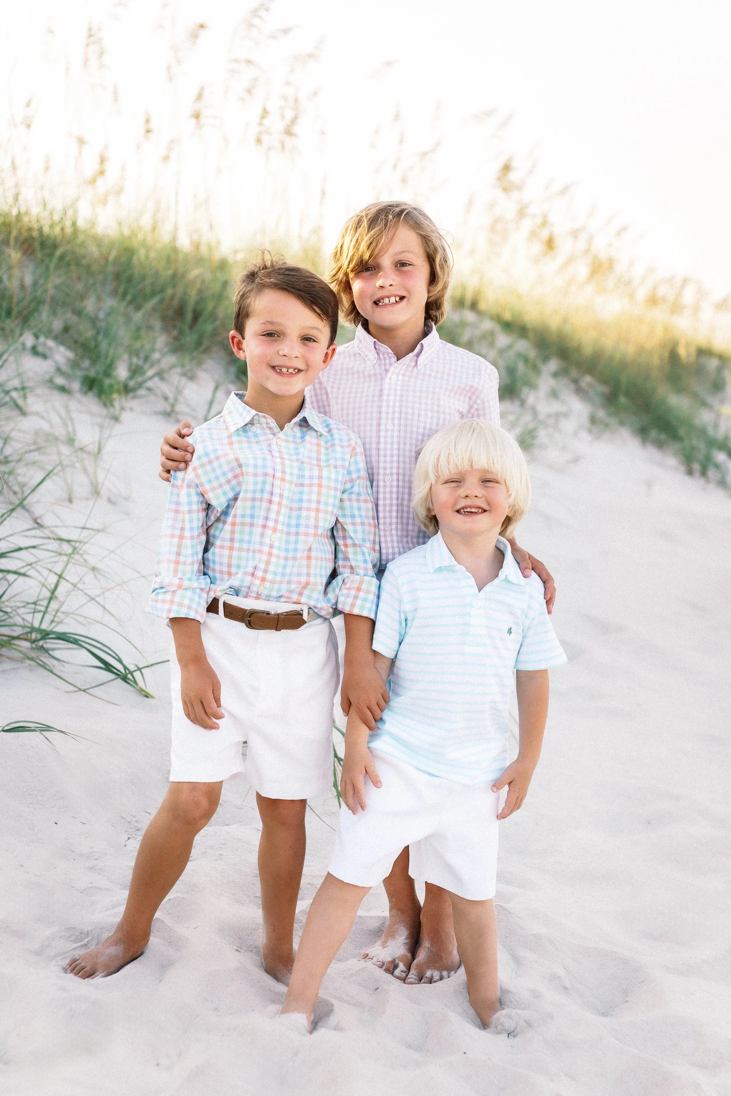 Four boys standing on the beach, smiling, with sand and grass in the background.Photographer Amelia Island, Jacksonville, St Augustine, St Simons Island, Savannah photographer