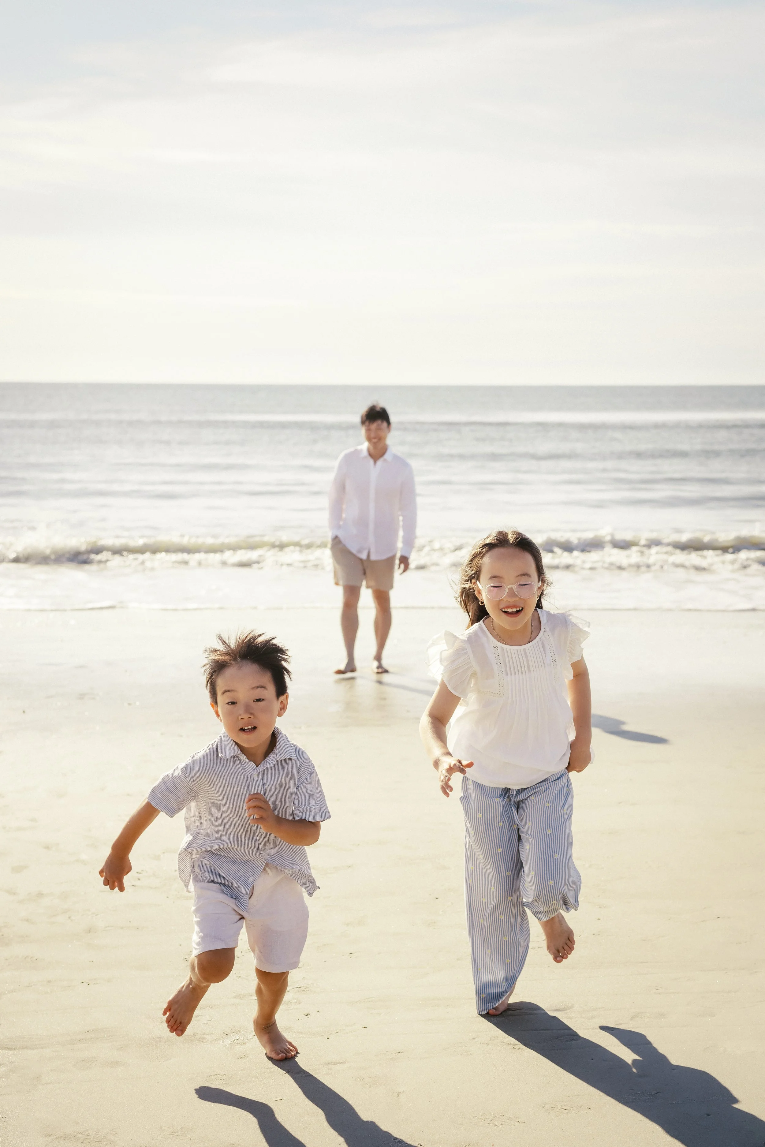 A group of children running on a sandy beach with the ocean in the background under a partly cloudy sky.Photographer Amelia Island, Jacksonville, St Augustine, St Simons Island, Savannah photographer