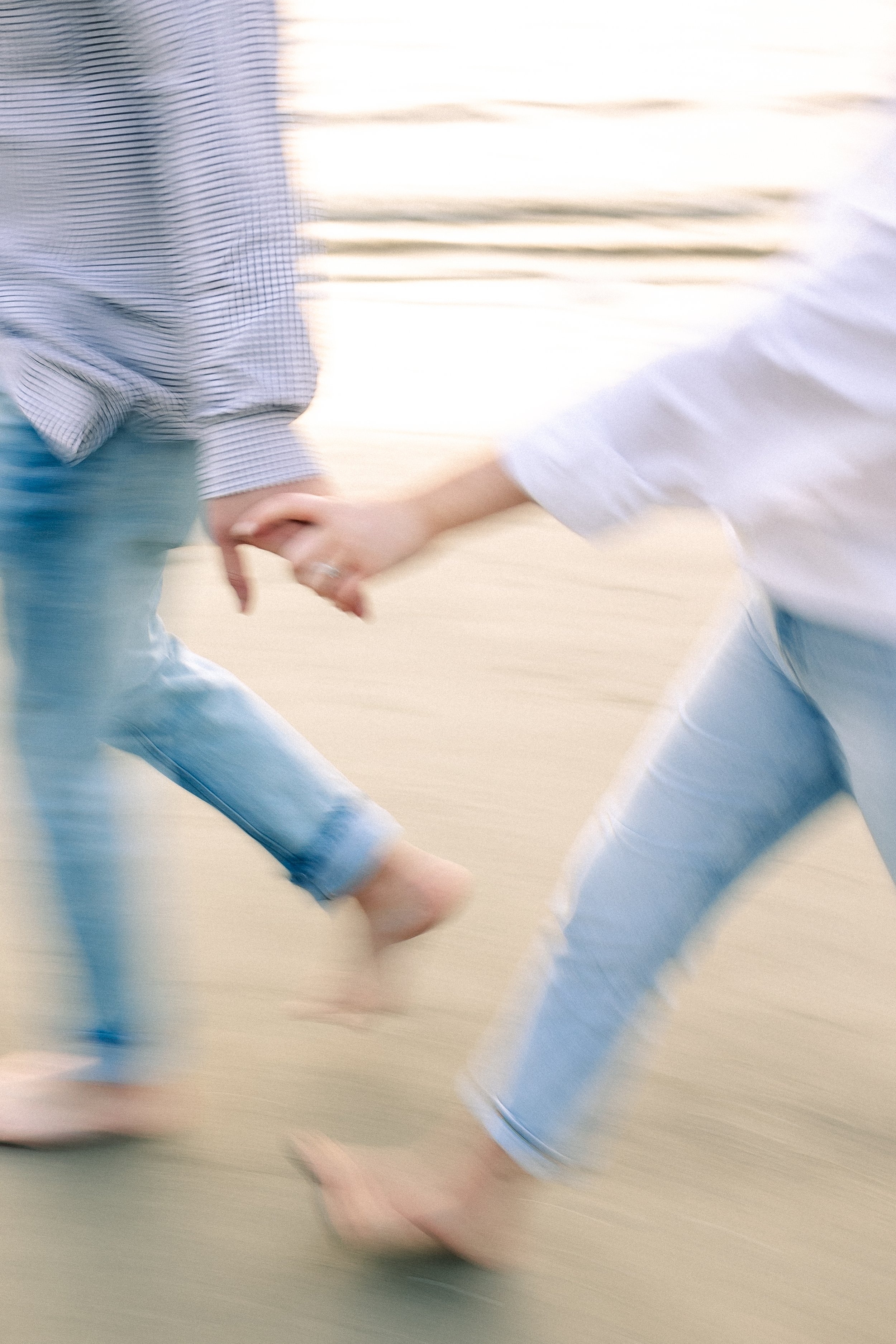 Two people holding hands while running or jumping, with a blurred background.