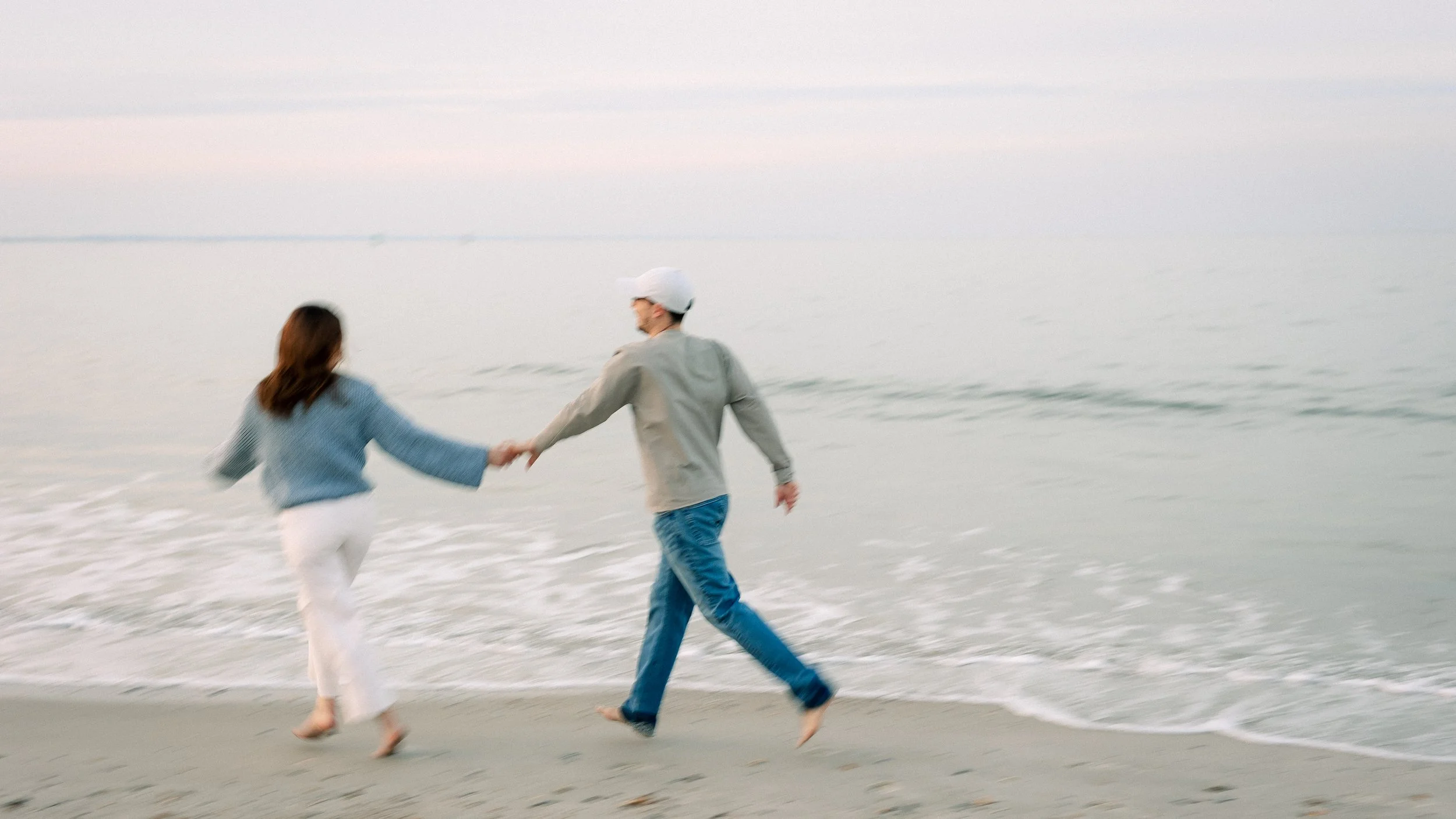 A couple holding hands and running along the shoreline at the beach during sunset.