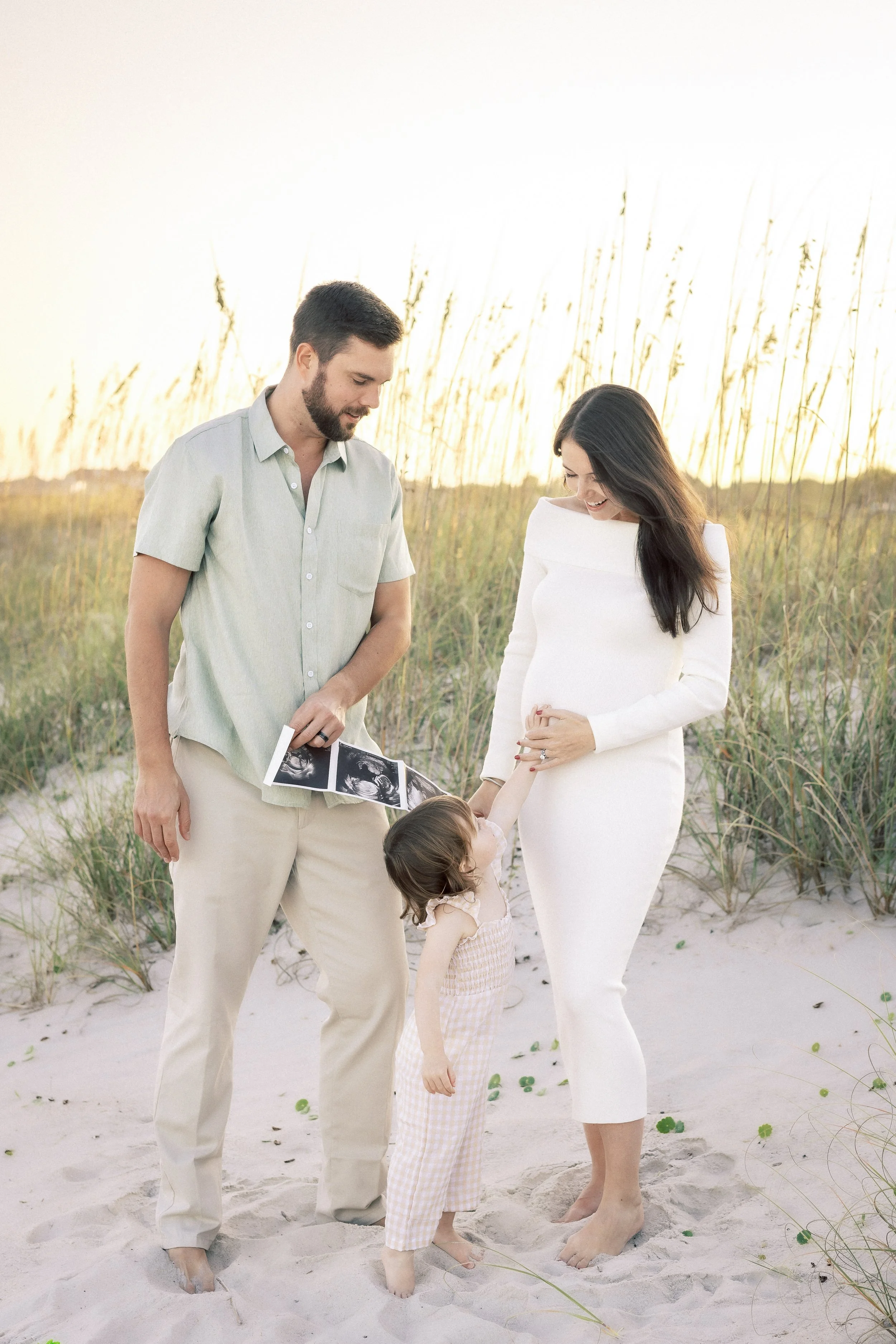 A family enjoying a moment on the beach. The father is holding ultrasound images, the mother is pregnant, and their two young children are holding hands with the mother.Photographer Amelia Island, Jacksonville, St Augustine, St Simons Island, Savanna