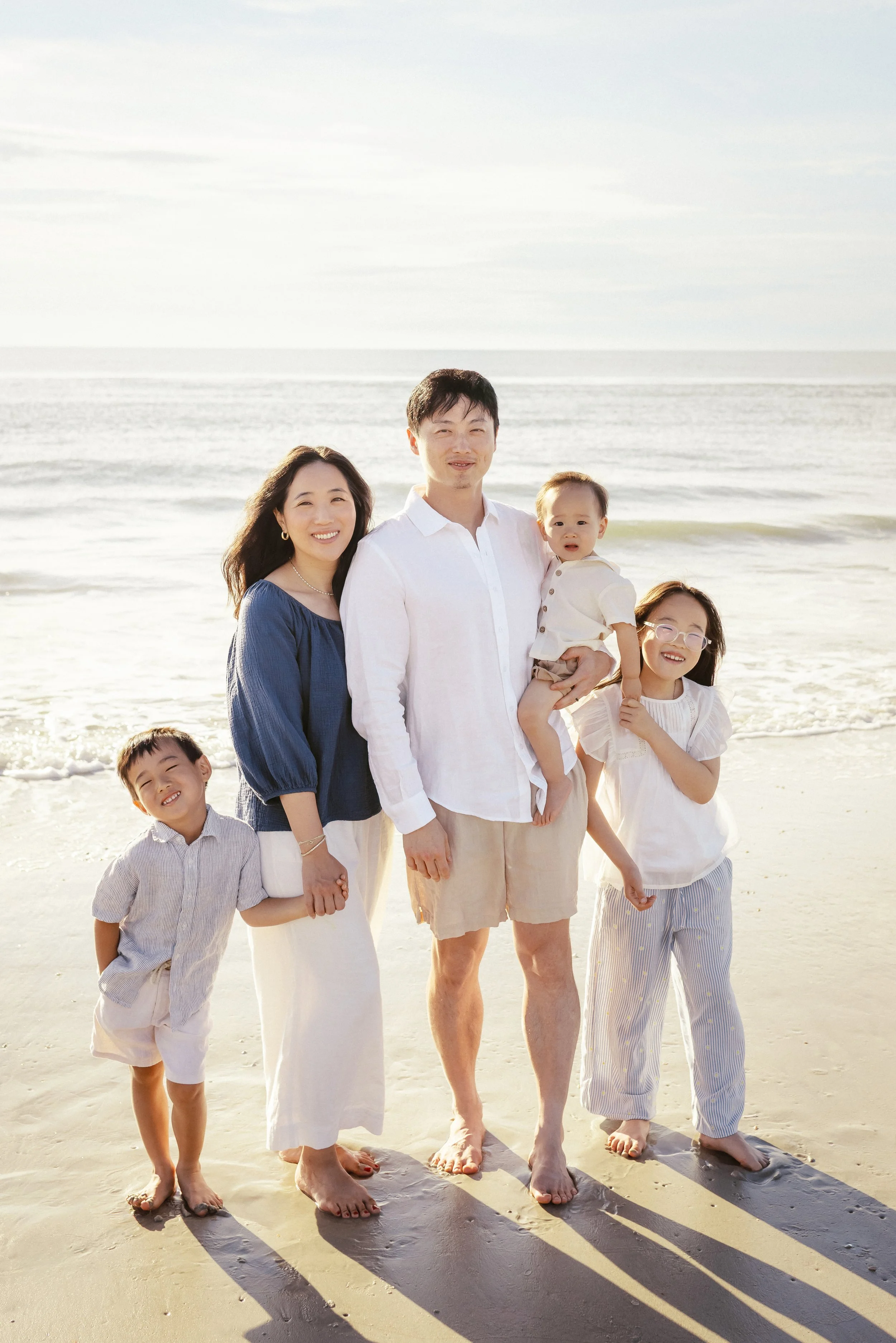 A family of six standing on a sandy beach, with the ocean and sky in the background. Photographer Amelia Island, Jacksonville, St Augustine, St Simons Island, Savannah photographer