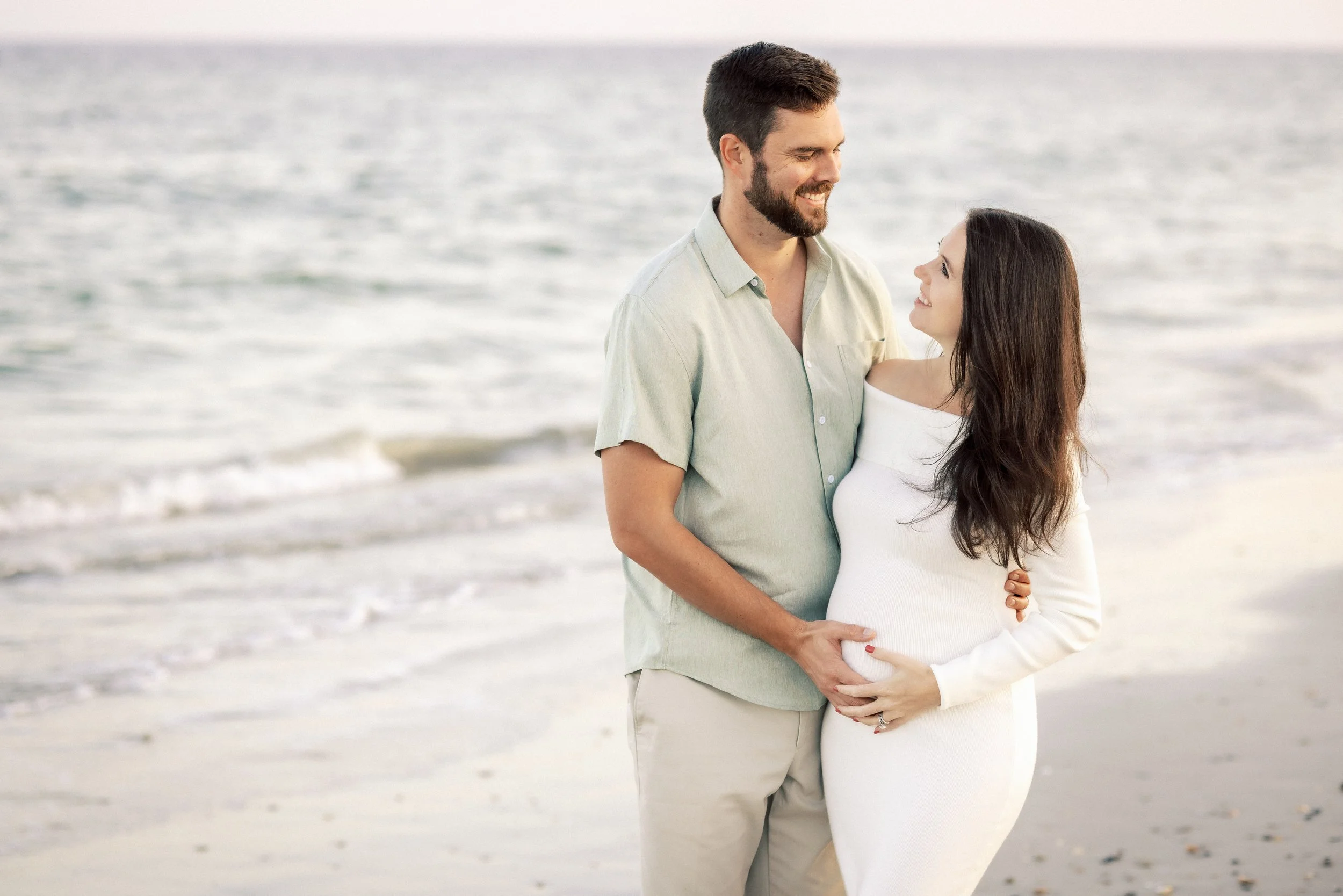 A smiling man and a pregnant woman standing on the beach, looking at each other.Photographer Amelia Island, Jacksonville, St Augustine, St Simons Island, Savannah photographer