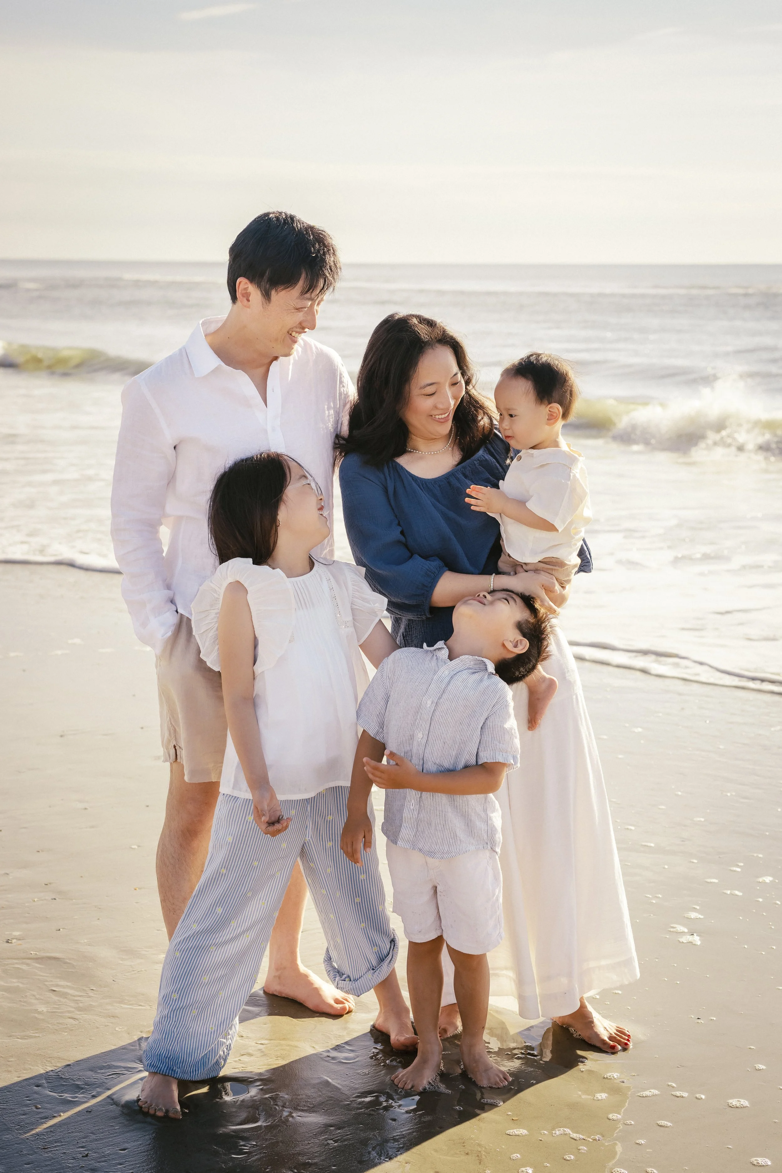 A happy family of six, including two adults and four children, standing on a beach near the shoreline with waves in the background. Photographer Amelia Island, Jacksonville, St Augustine, St Simons Island, Savannah photographer
