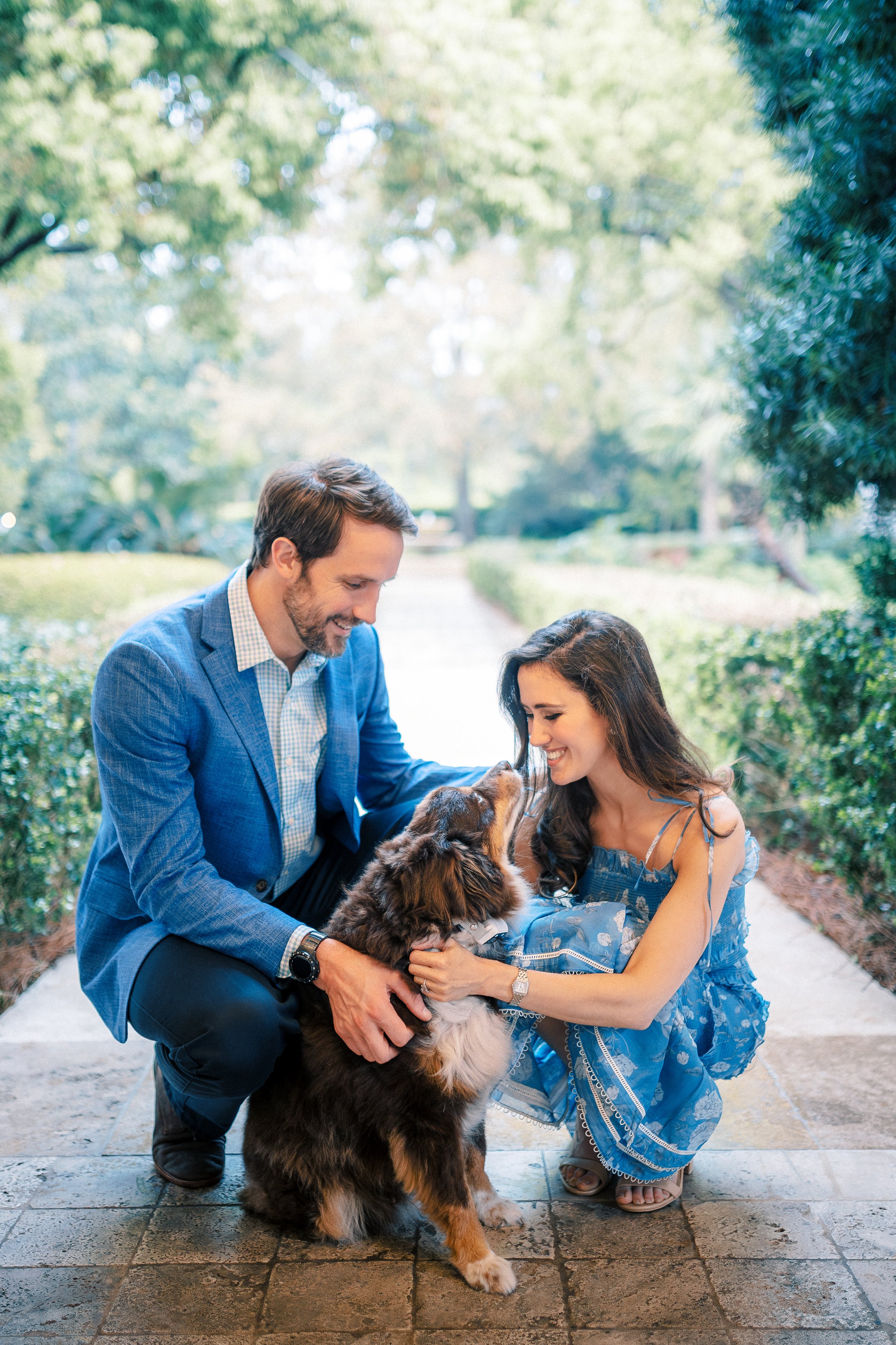 A man and a woman are outdoor, smiling, and petting a large, fluffy dog.
