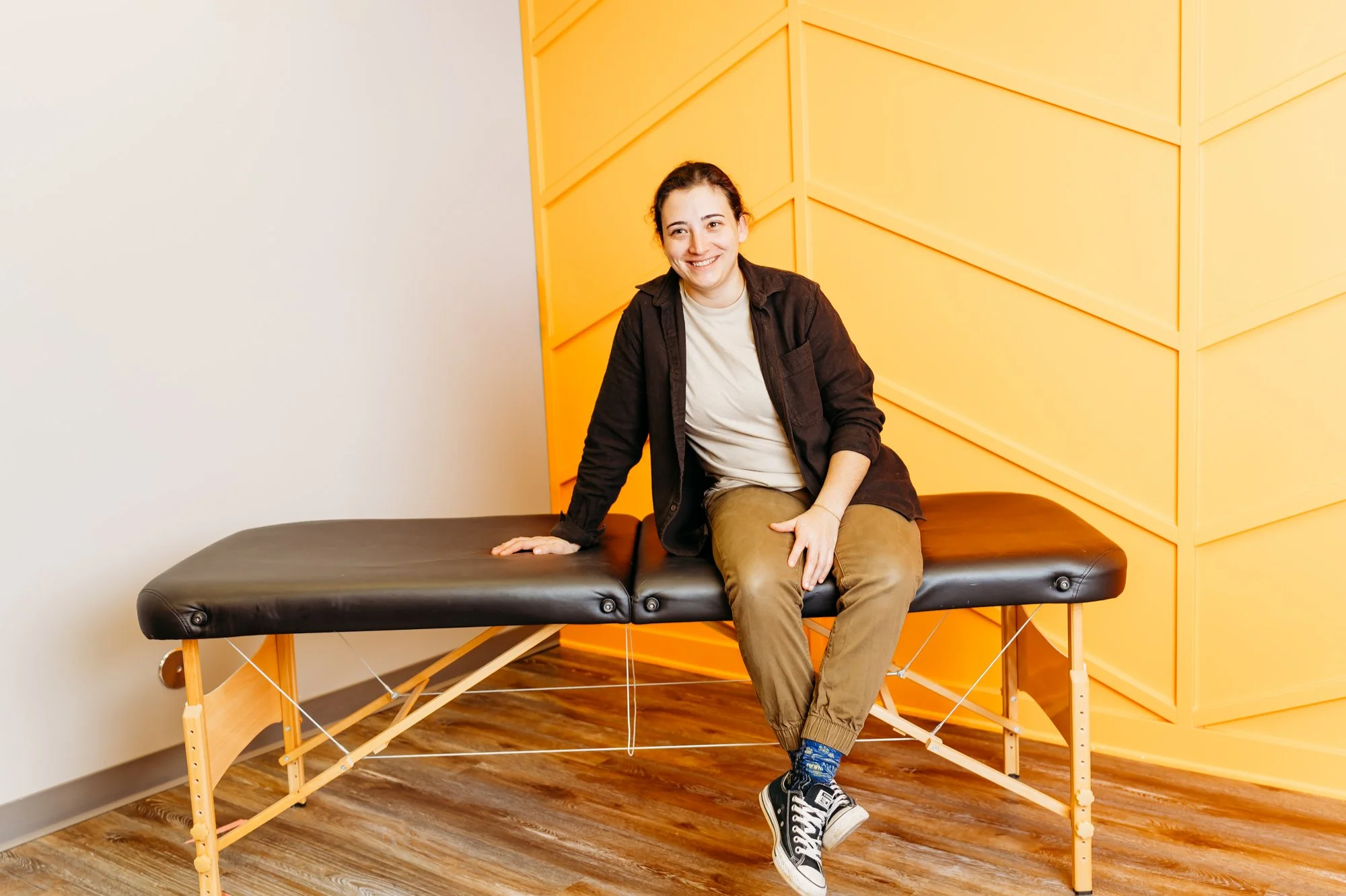 Dr. Gabi Dejuliis smiling and sitting on a physical therapy table in her pediatric clinic