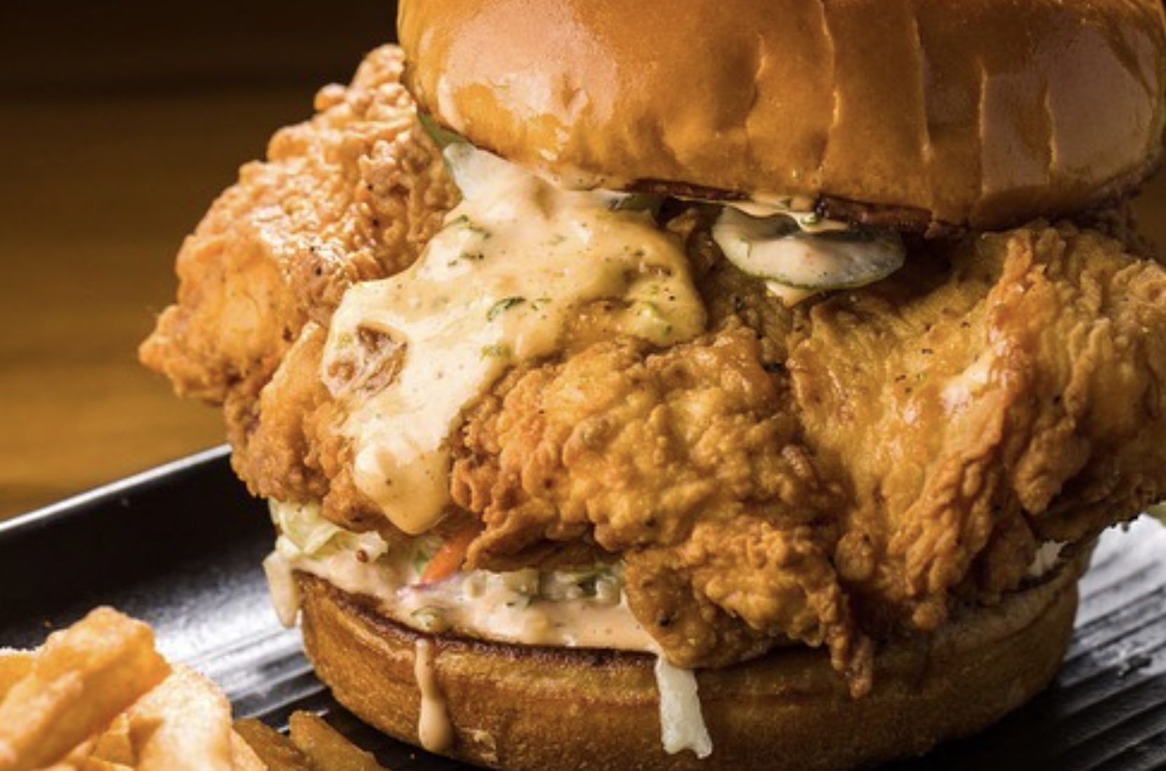 Close-up of a fried chicken sandwich with fried chicken fillets, coleslaw, melted cheese, pickles, and a toasted bun.