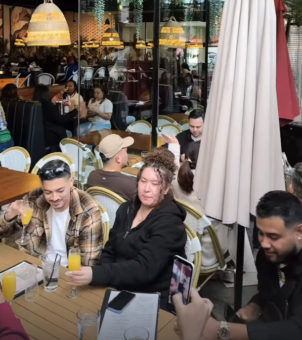 People enjoying drinks at an outdoor cafe with decorative hanging lights inside.