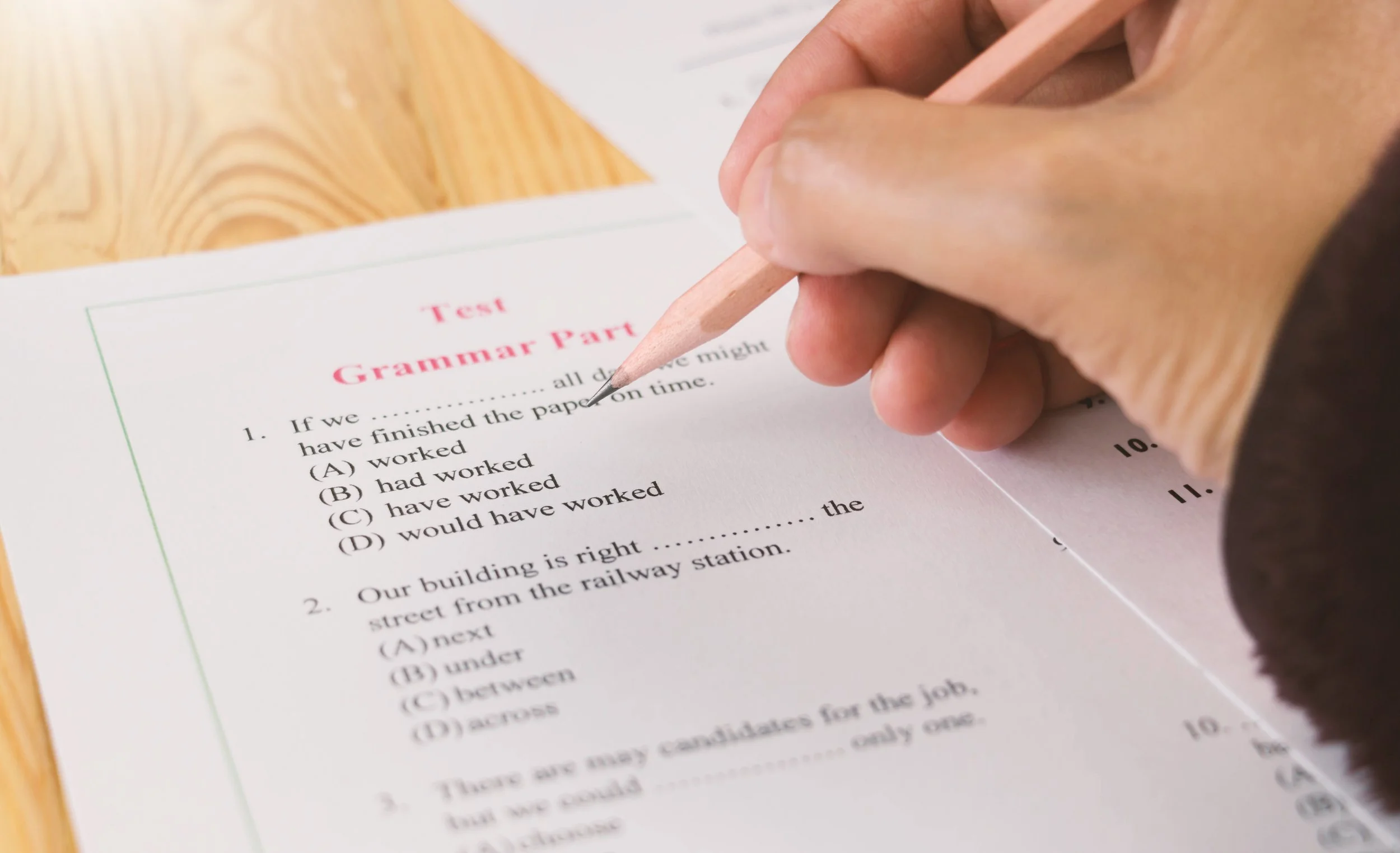 Close-up of a person holding a pencil above a grammar test page on a wooden table