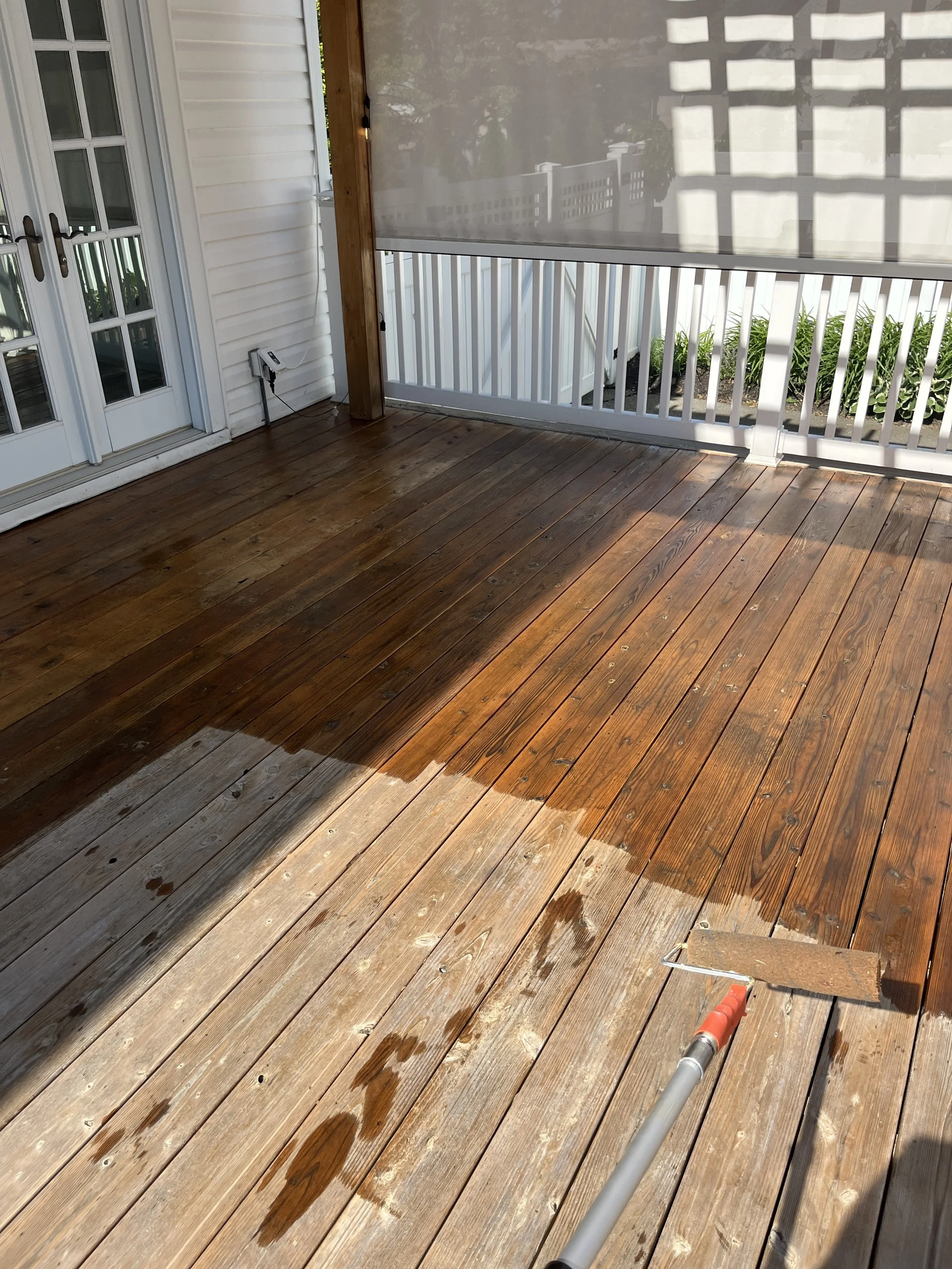 A wooden deck being power washed, with water spraying across the surface, and a water spray nozzle at the bottom right corner.