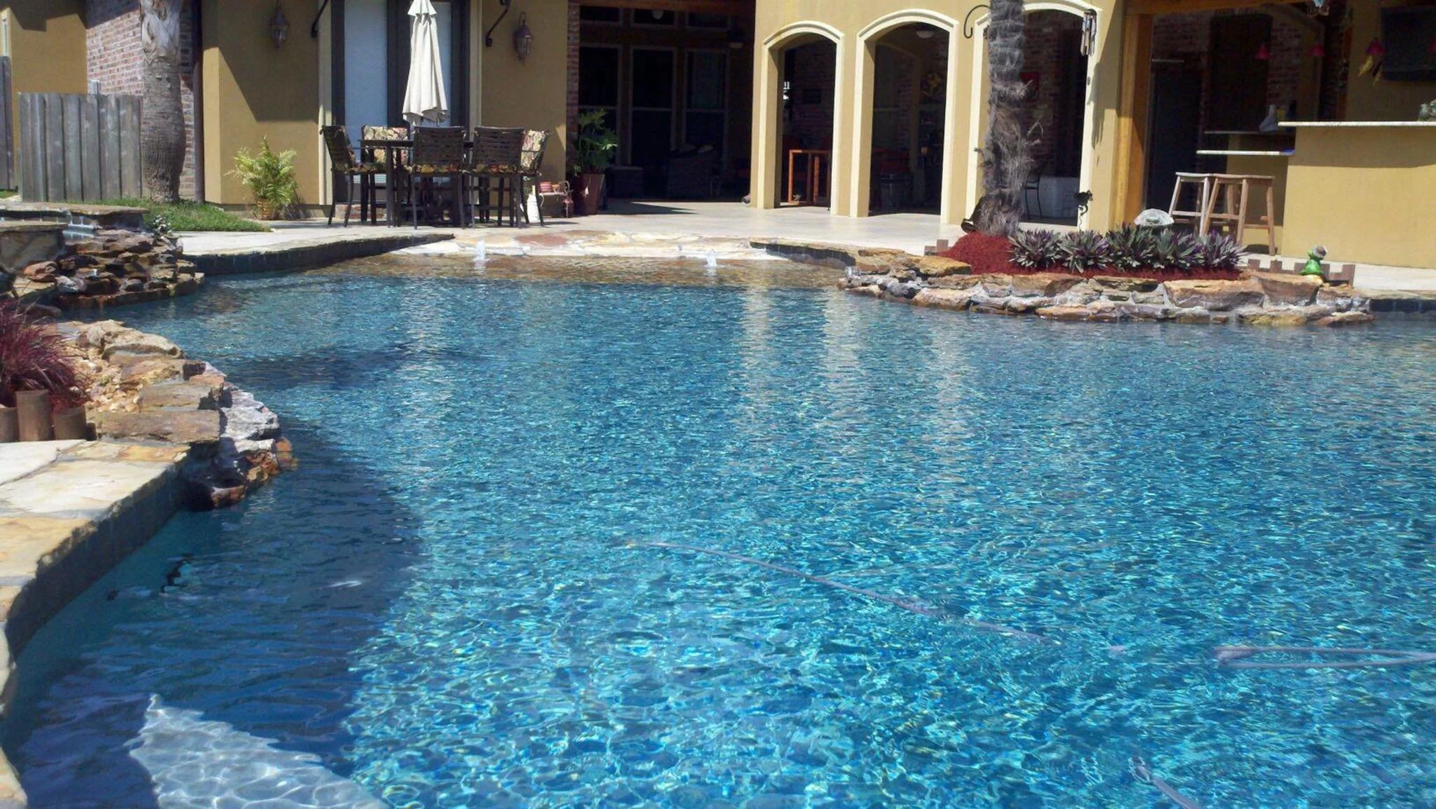 Custom-designed freeform residential pool with rock waterfall, waterslide, hot tub, zero entry in Baton Rouge built by Gulf South Pools & Outdoors.