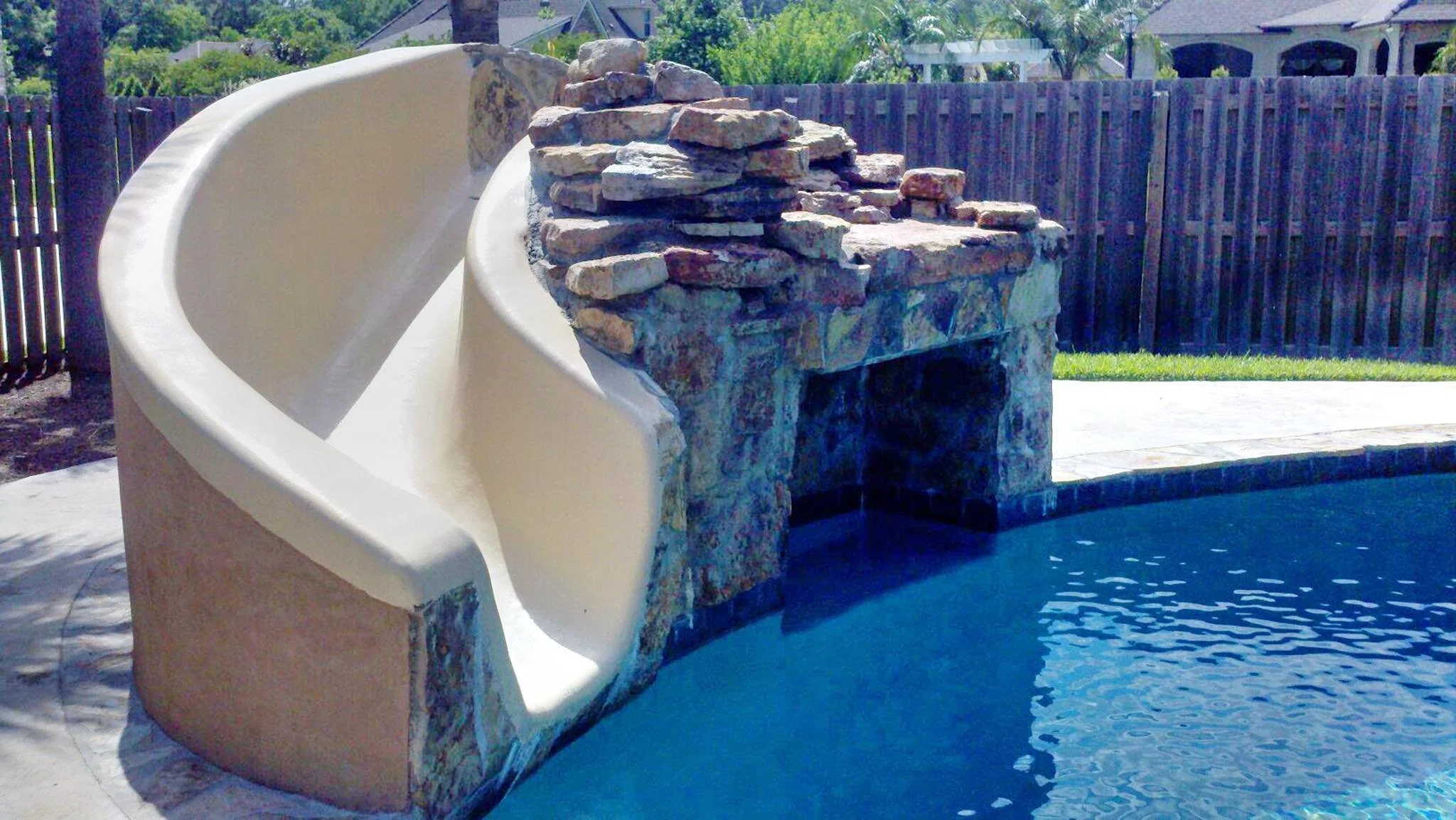 Custom-designed freeform residential pool with rock waterfall and waterslide in Baton Rouge built by Gulf South Pools & Outdoors.