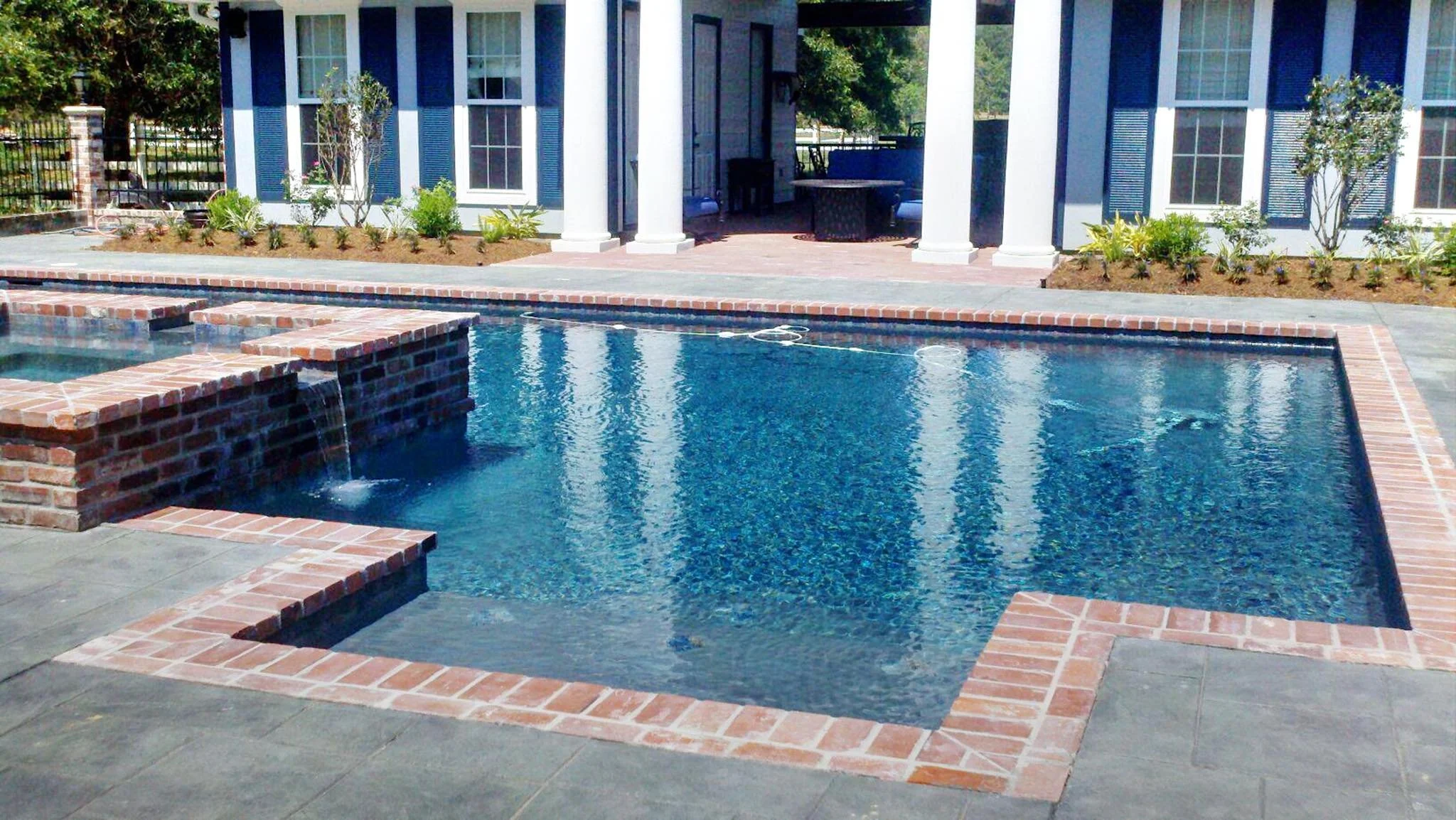 Custom-designed geometric residential pool with waterfall and hot tub in Baton Rouge built by Gulf South Pools & Outdoors.