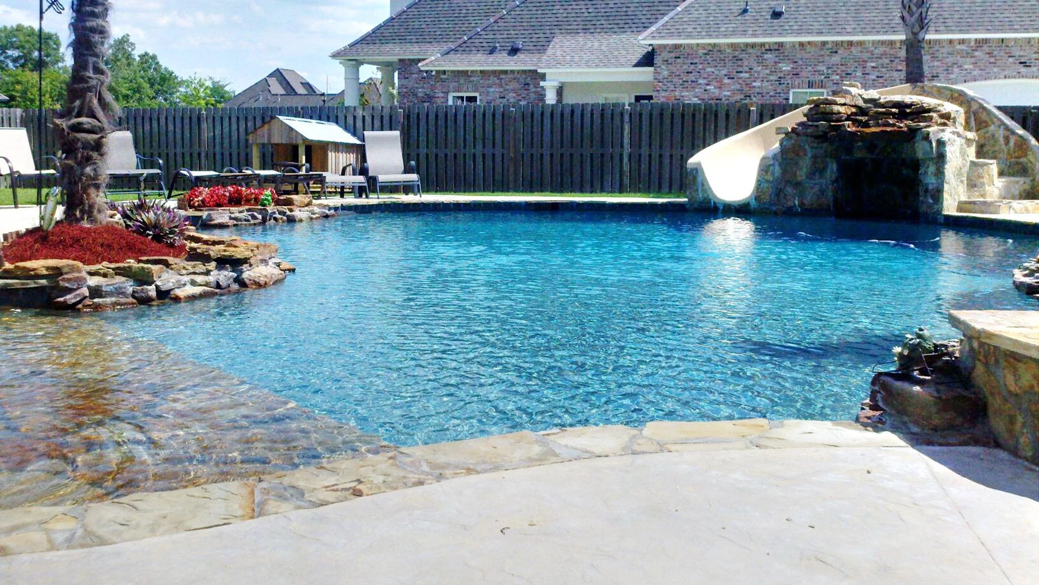 Custom-designed freeform residential pool with rock waterfall, waterslide, hot tub, zero entry in Baton Rouge built by Gulf South Pools & Outdoors.