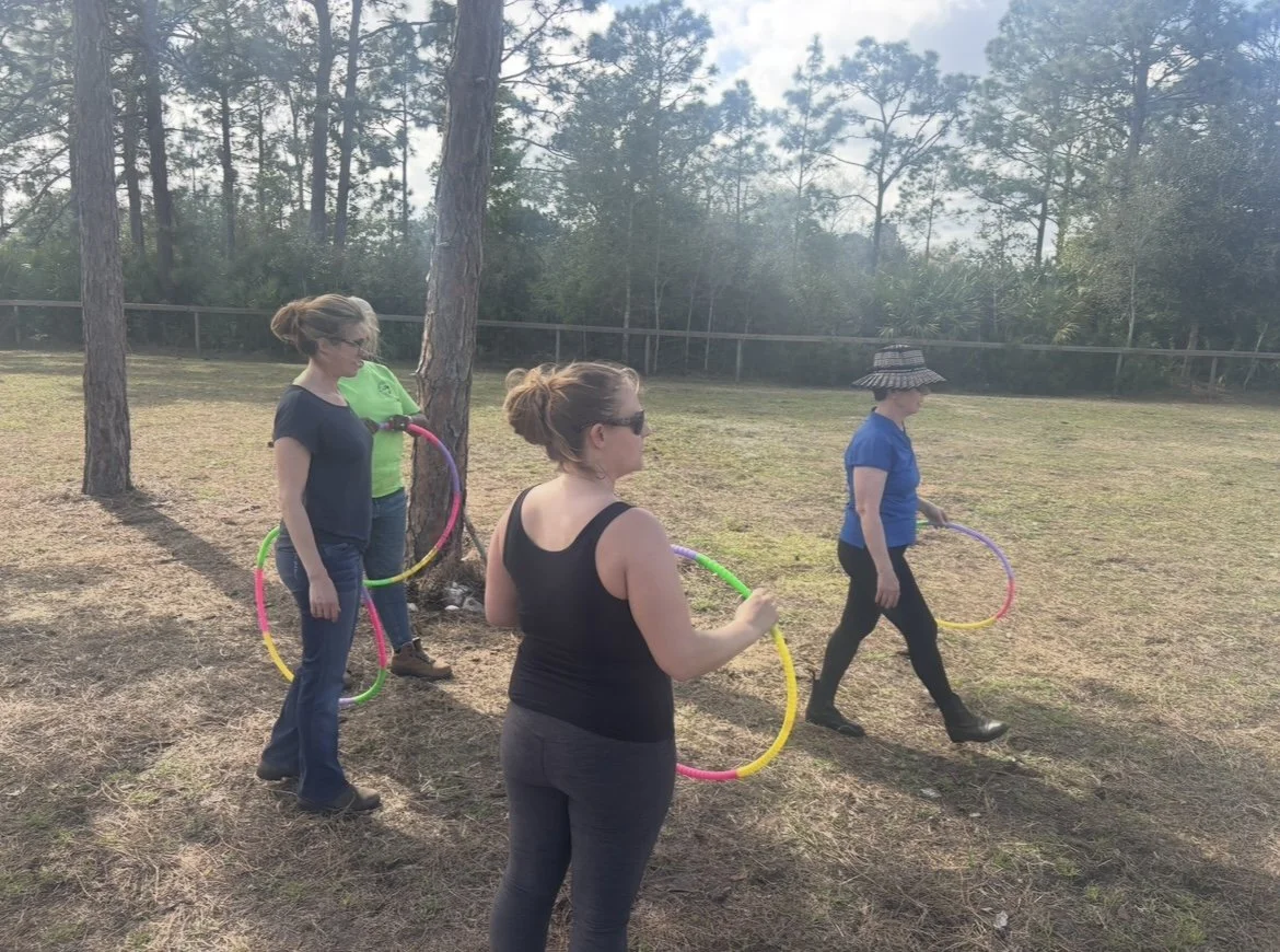 4 people looking at a horse, not in the picture, holding hoops for the horse