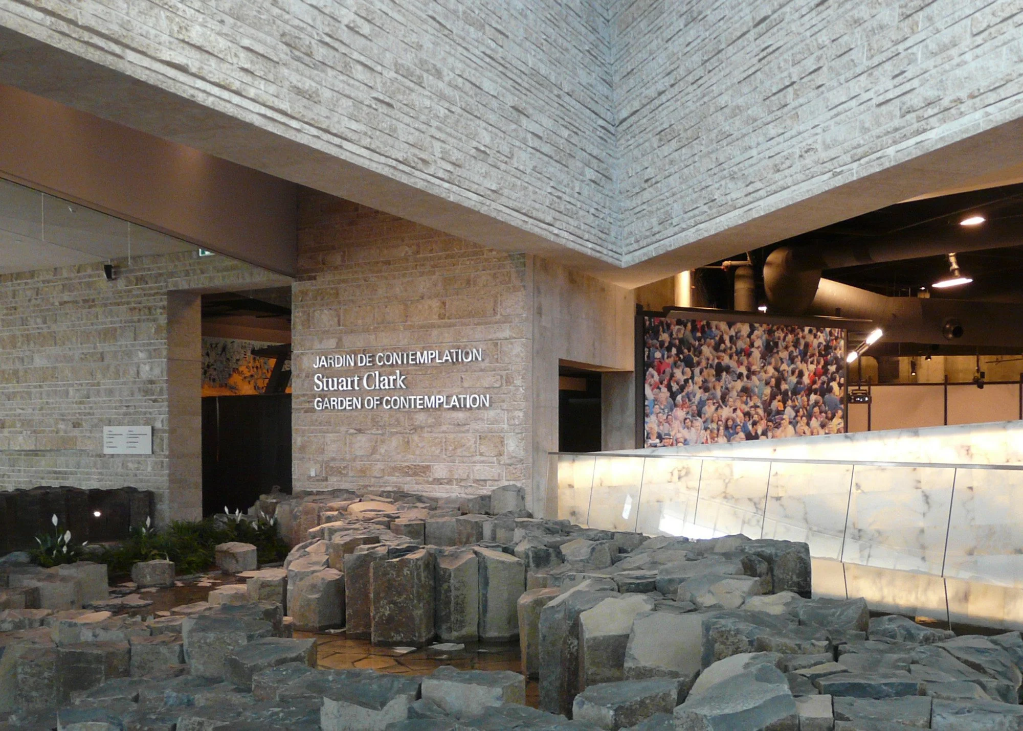 Interior view of the Garden of Contemplation at the San Francisco Museum of Modern Art, featuring rocks, plants, and a large crowd photo display.