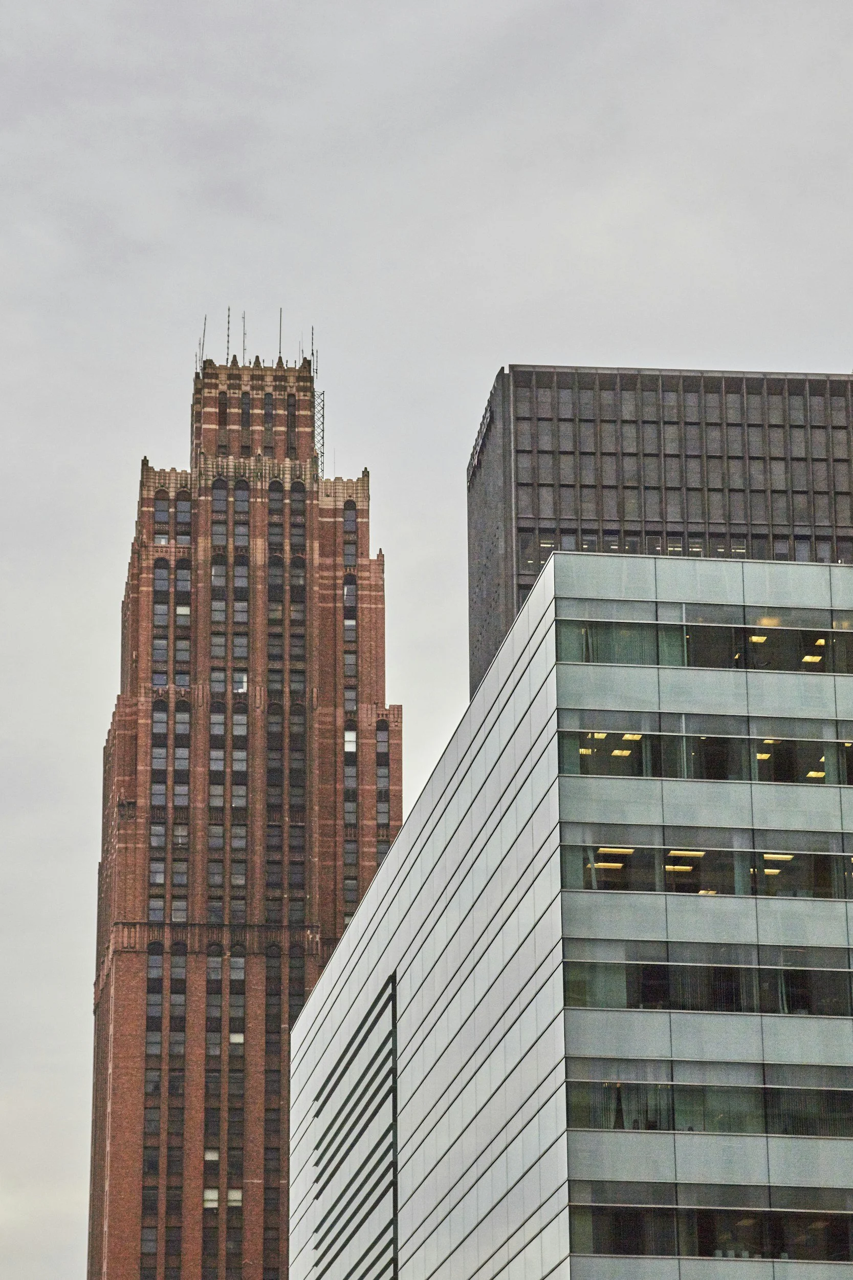 A cityscape showing a tall, brick, gothic-style skyscraper with a modern glass building in front.