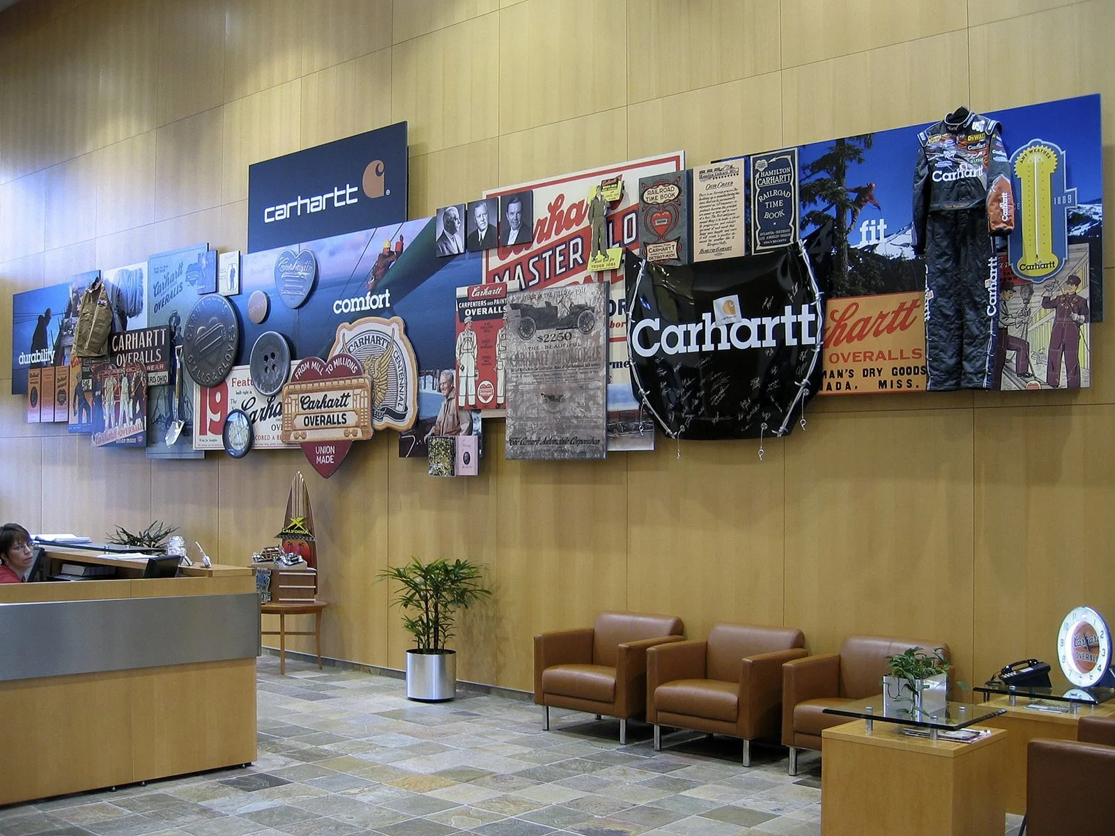 Interior of a Carhartt showroom or office with vintage advertisements, memorabilia, and clothing displays on the wall, with seating and a reception desk.