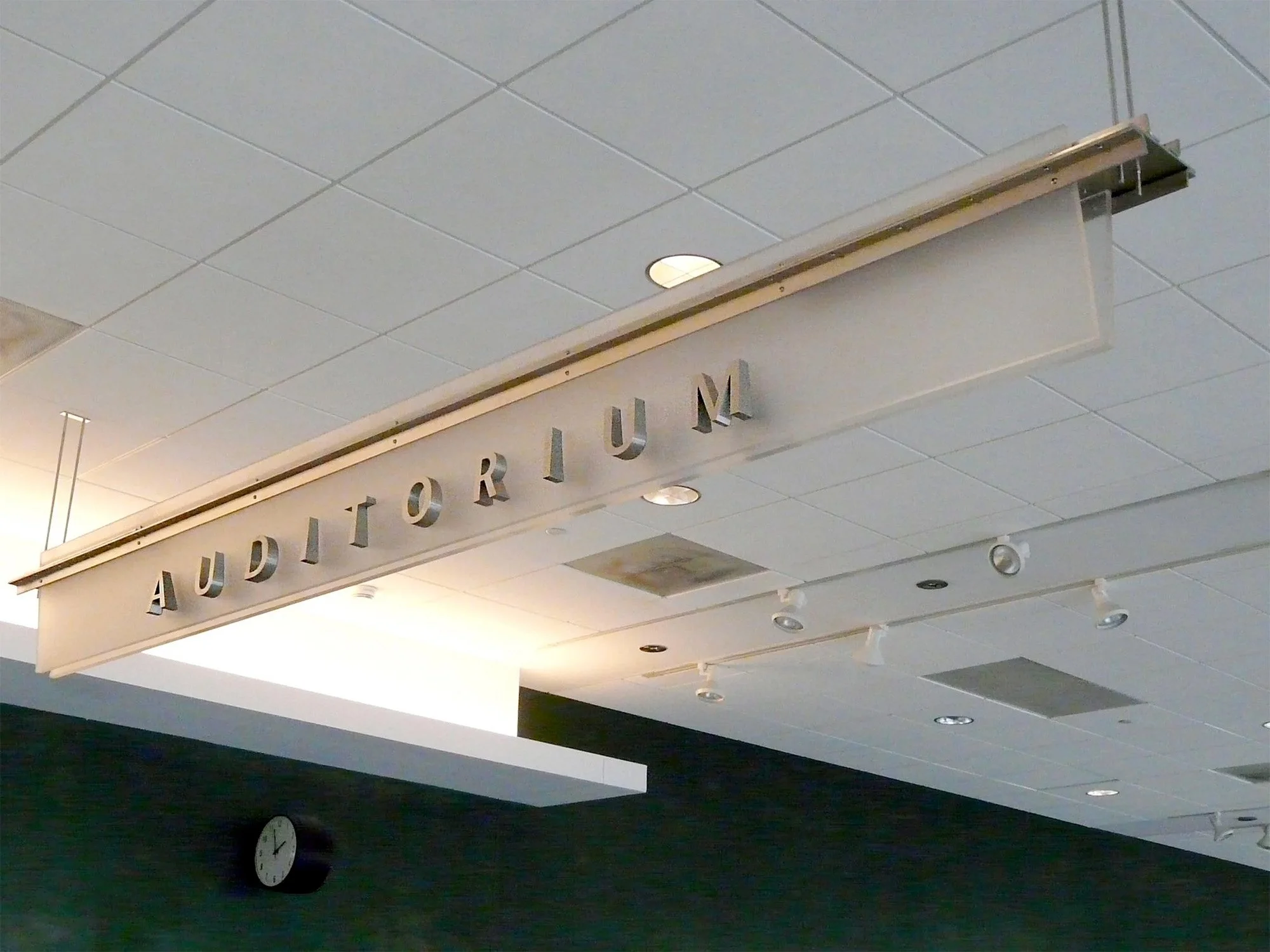 A sign with the word 'AUDITORIUM' hanging from the ceiling of an indoor space.