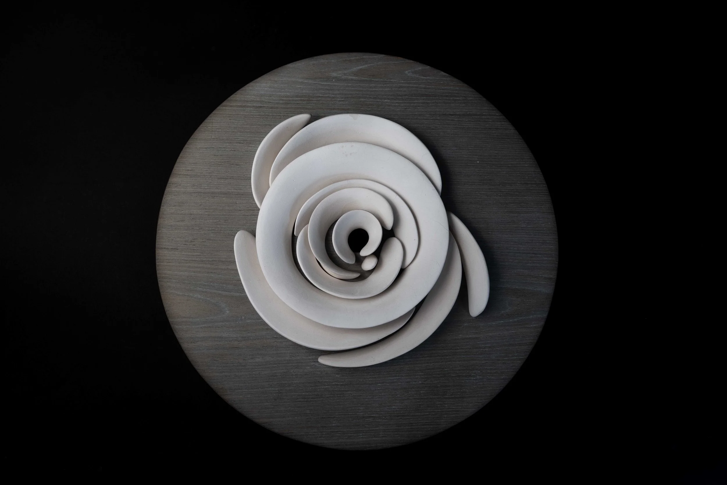 Top-down view of a decorative white spiral sculpture on a round gray wooden surface against a black background.
