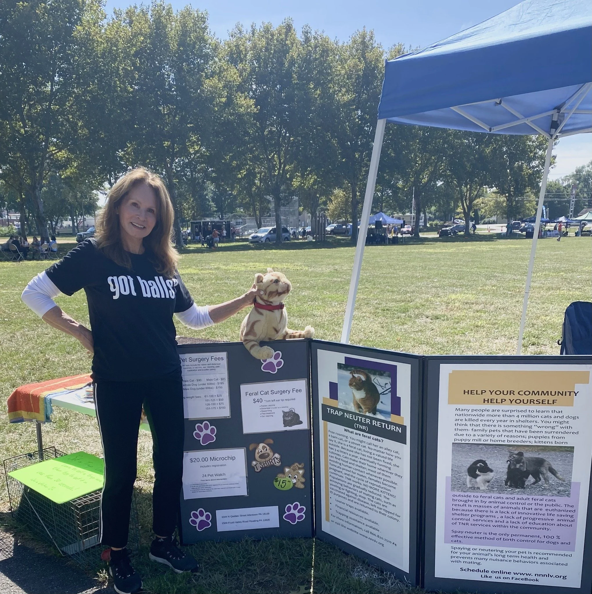 Woman at pet adoption event with a plush dog toy, standing next to an informational display about feral cat surgery fees and trap-neuter-return programs