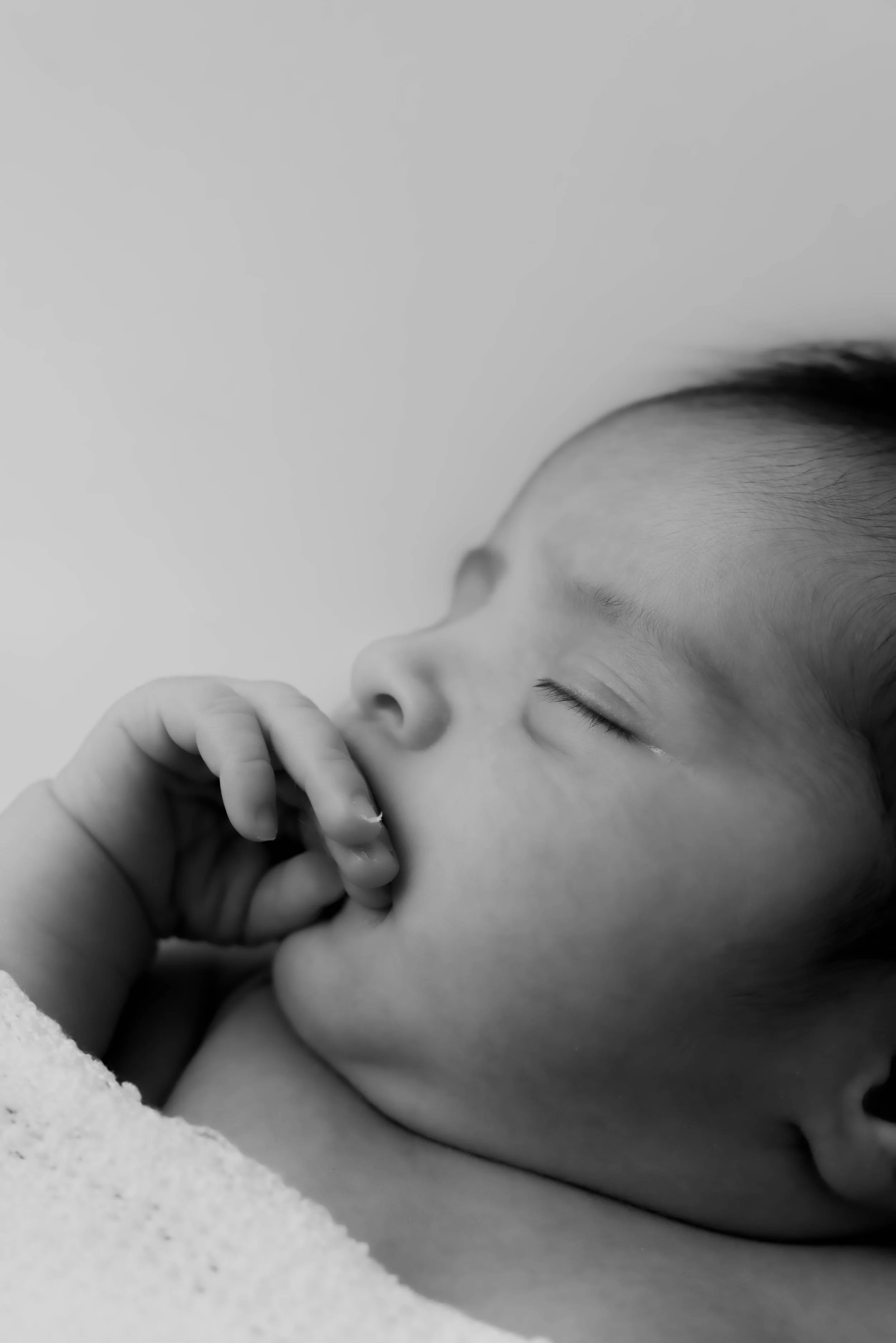 Close-up of a sleeping young child with closed eyes, resting head on a surface, and hand near mouth.