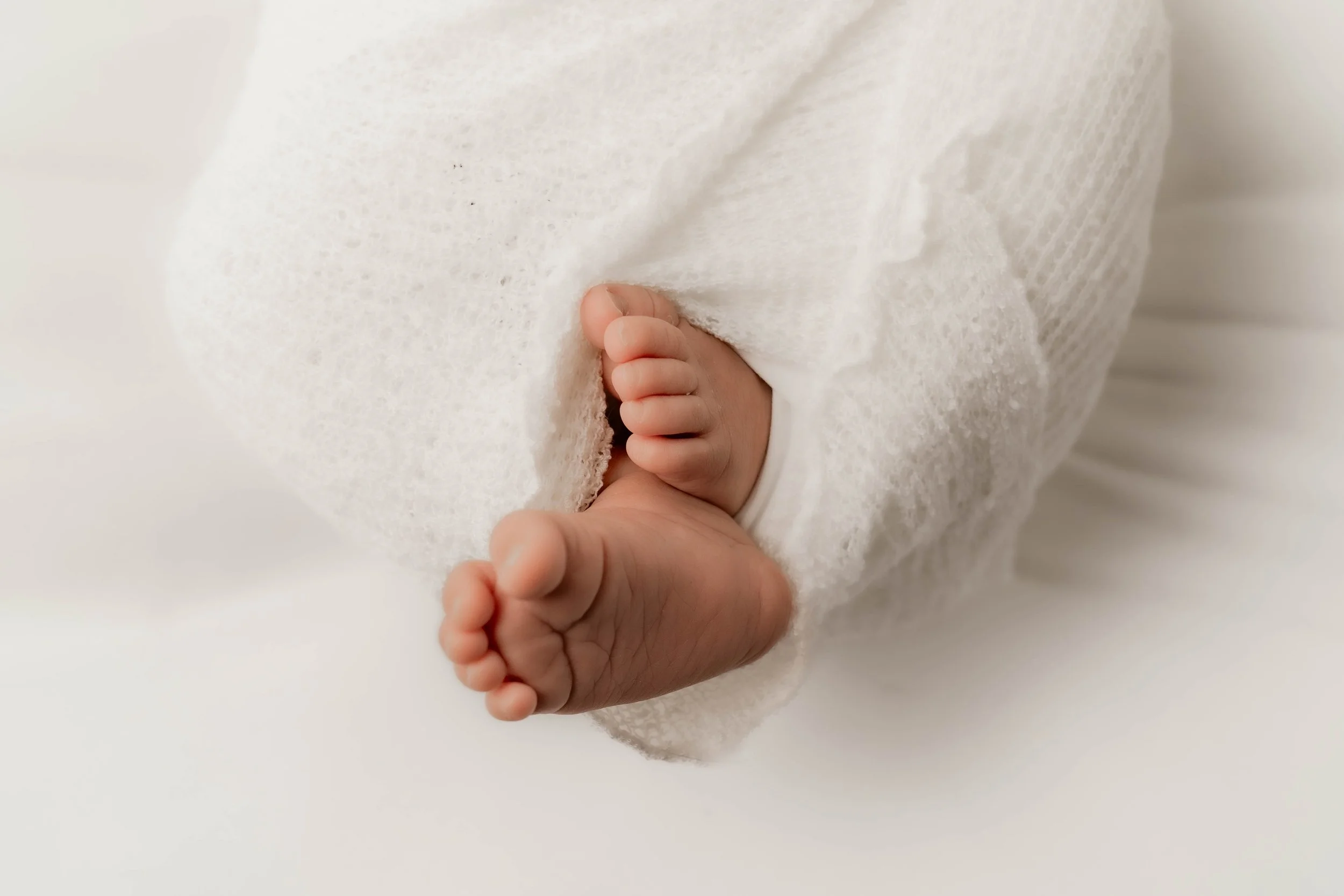 Close-up of a newborn baby's tiny feet wrapped in white cloth.